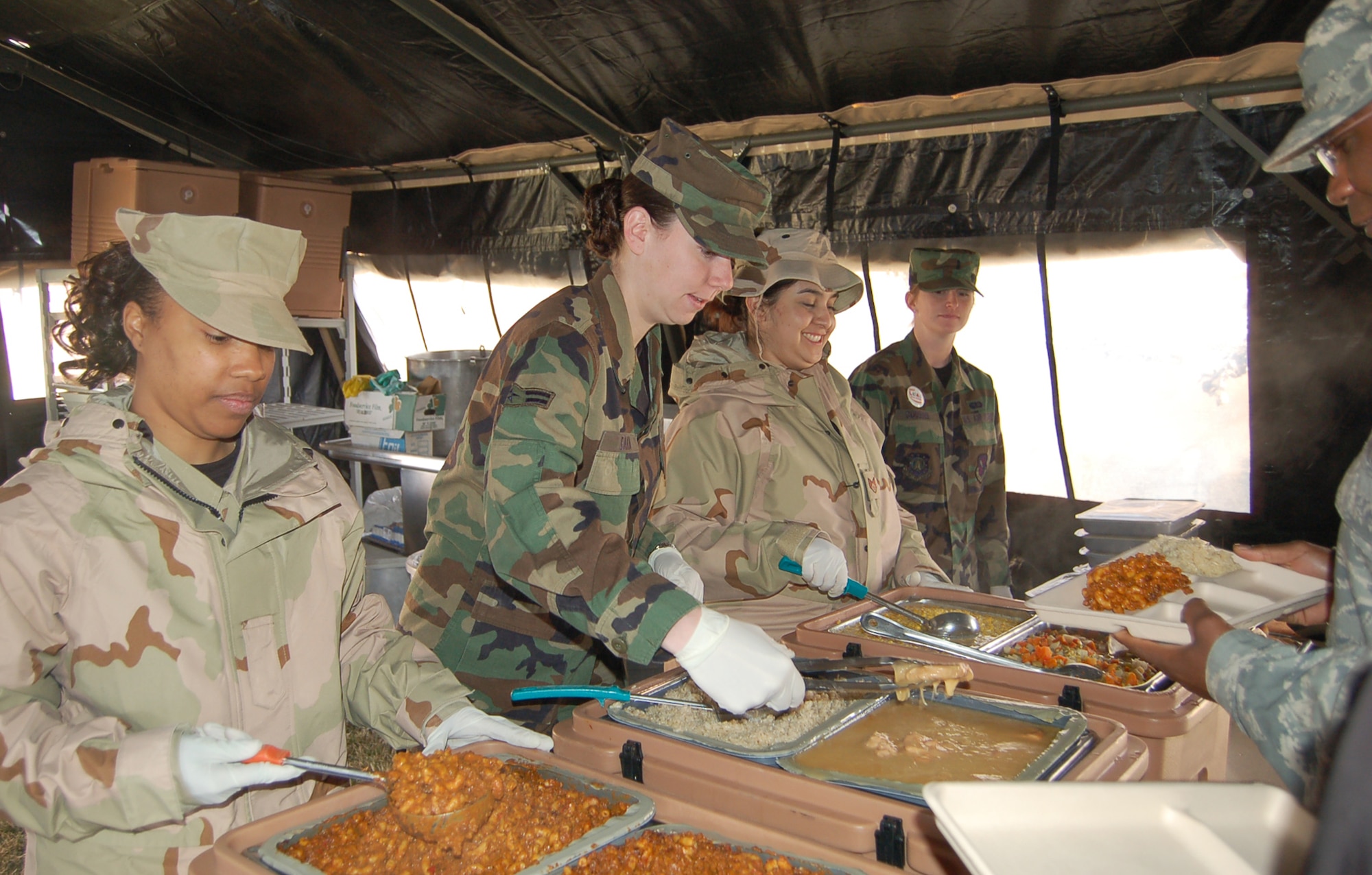 Staff Sgt. Racquel Merriam and Airman 1st Class Tiffany Eakin, 21st Services Squadron, dish up food for guests at an expeditionary lunch April 9. The 21st SVS team prepared Unitized Group Rations, or UGRs, for the crowd using only a vat of boiling water. (U.S. Air Force photo/Corey Dahl) 