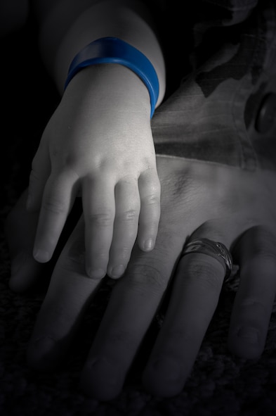 MOODY AIR FORCE BASE, Ga.-- An Airman holds the hand of a child wearing a blue bracelet symbolizing Child Abuse Prevention Month here April 16. Four children die every day in the United States as a result of child abuse. (U.S. Air Force photo illustration by Airman 1st Class Brittany Barker)