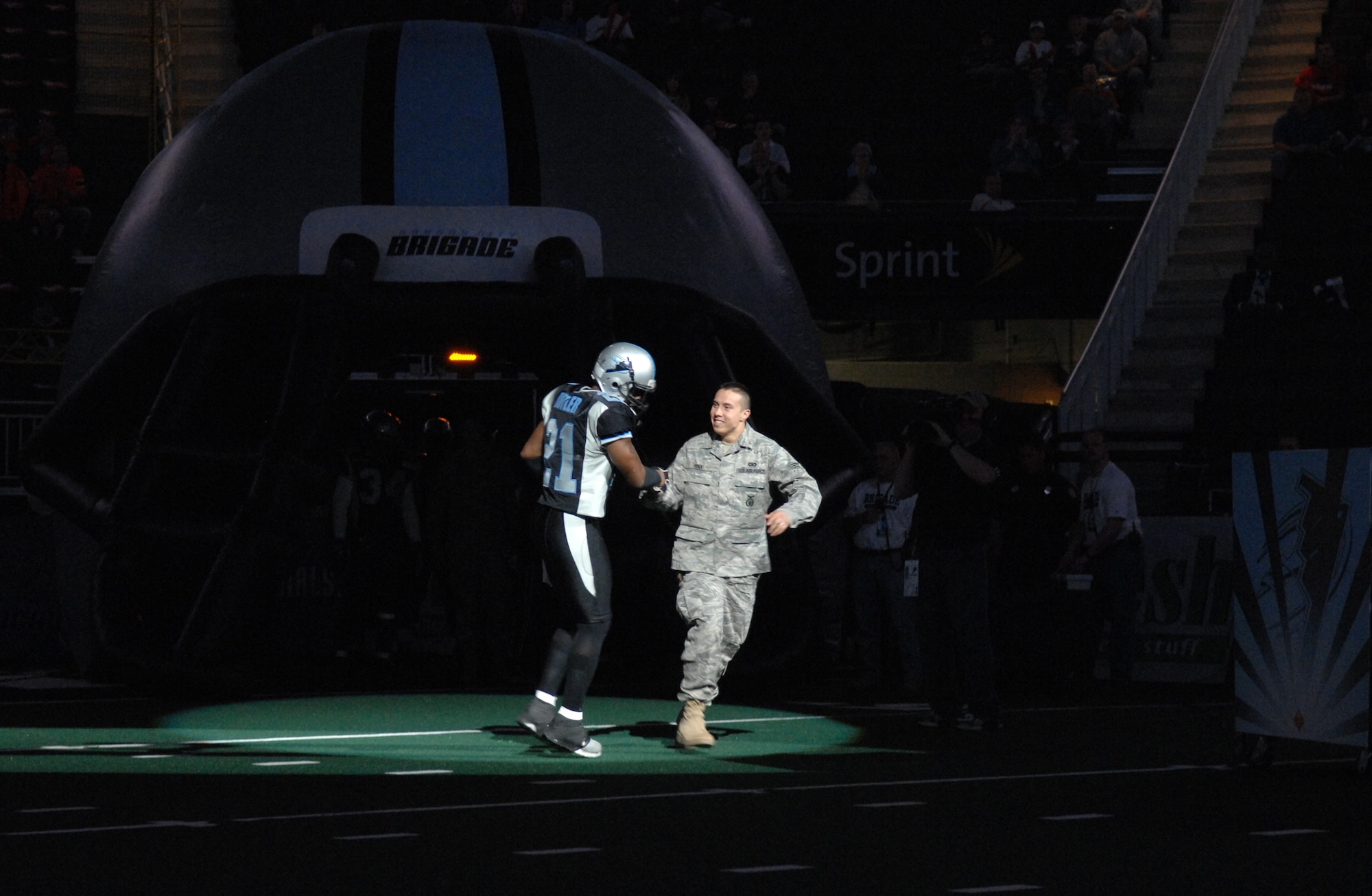 KANSAS CITY, Mo. – Senior Airman John Pena, 509th Security Forces, runs onto the field at the Sprint Center with a Kansas City Brigade player April 14. The Kansas City Brigade (0-6) lost 49-42 to the Chicago Rush (5-2). The Kansas City Brigade is a team from the Arena Football League. The team got their name Nov. 21, 2005, when the AFL announced the team would be called the Kansas City Brigade.  The team then decided to model their team logo after the B-2. (U.S. Air Force photo/Airman 1st Class Stephen Linch)

