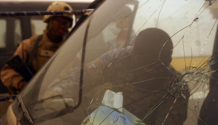 An Iraqi guard searches a vehicle while Cpl. Gerald Suazo, the corporal of the guard for entry control point one, is serving an overwatch position for the guards and Iraqi Police. Coalition forces are transitioning the security role to Iraqis so they can eventually perform these duties with little or no assistance.