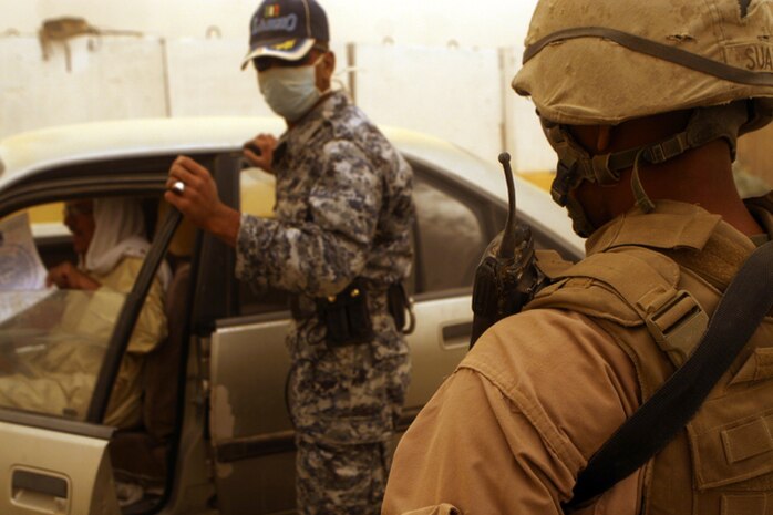Cpl. Gerald Suazo (right), the corporal of the guard for entry control point one with 3rd Battalion, 6th Marine Regiment, Regimental Combat Team-1 watches an Iraqi Police officer conduct a vehicle search at ECP-1, April 17. Iraqi Police and guards are responsible for checking vehicles and pedestrians before entering Fallujah, taking a larger role for the security of the Iraqi people.