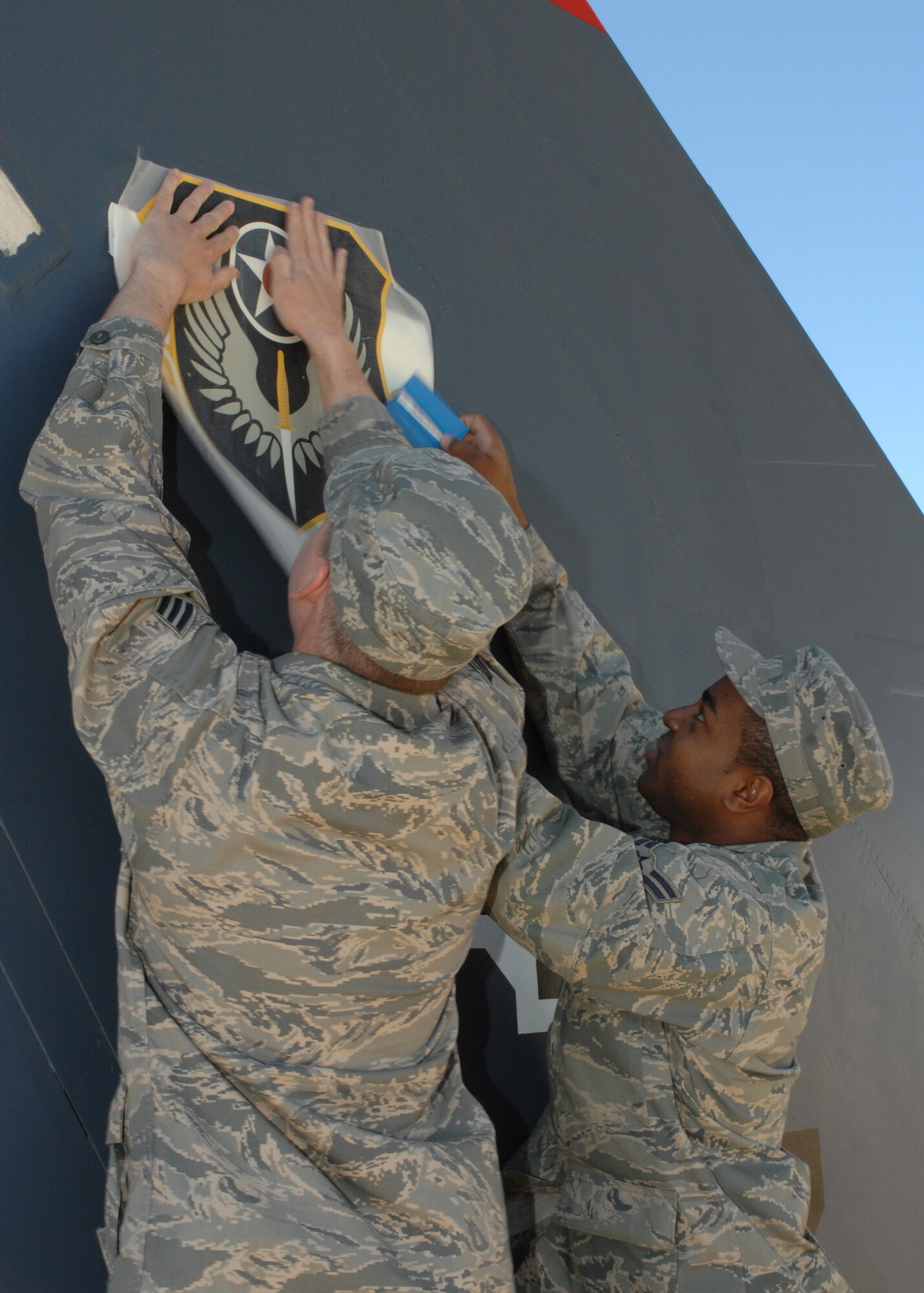 CANNON AIR FORCE BASE N.M. - Senior Airman Nicholas Schmidt, 27th Special Operations Aircraft Maintenance Squadron, and Airman 1st Class Stephen Johnson, 27th Special Operations Maintenance Operations Squadron, press the Air Force Special Operations Command emblem onto the tail fin in front of the Landing March 27. The tail fin needing a replacement emblem was to the back of the tailfin on the right going to the Landing.  (U.S. Air Force photo by Airman 1st Class James R. Bell)