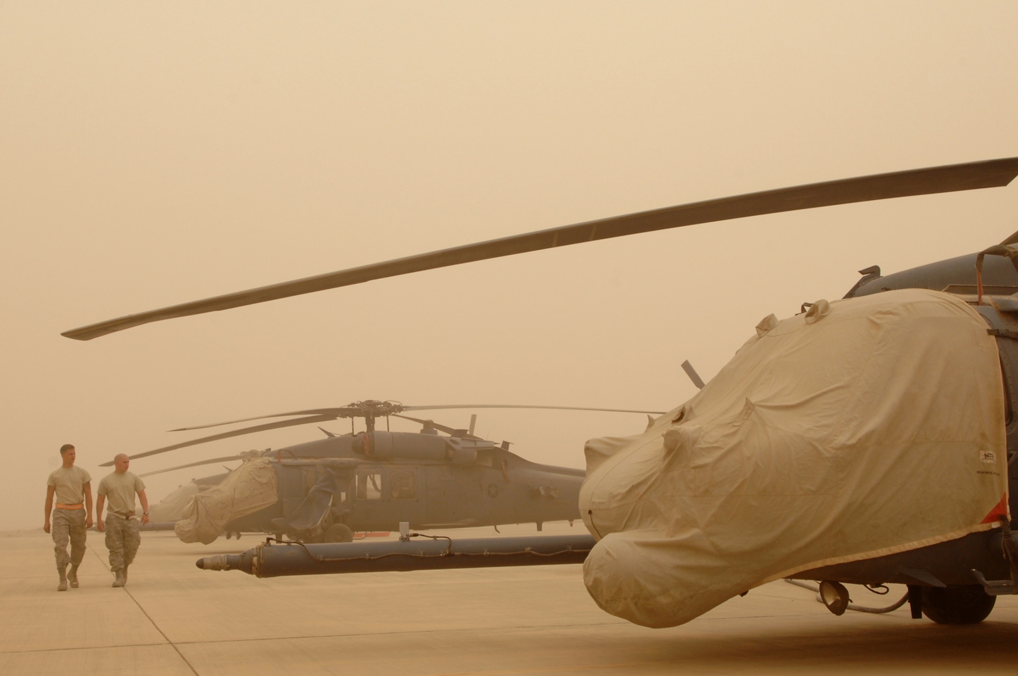 BALAD AIR BASE, Iraq -- Airman 1st Class Jason Schwenn and Senior Airman Caleb Castillo, 64th Expeditionary Helicopter Maintenance Unit crew chiefs, walk through a row of HH-60G Pavehawk helicopters during a major dust storm here, April 17. During extreme weather conditions, extra precautions are taken to protect aircraft from weather elements. Both Airmen are deployed from Moody Air Force Base, Ga. (U.S. Air Force photo/ Senior Airman Julianne Showalter)