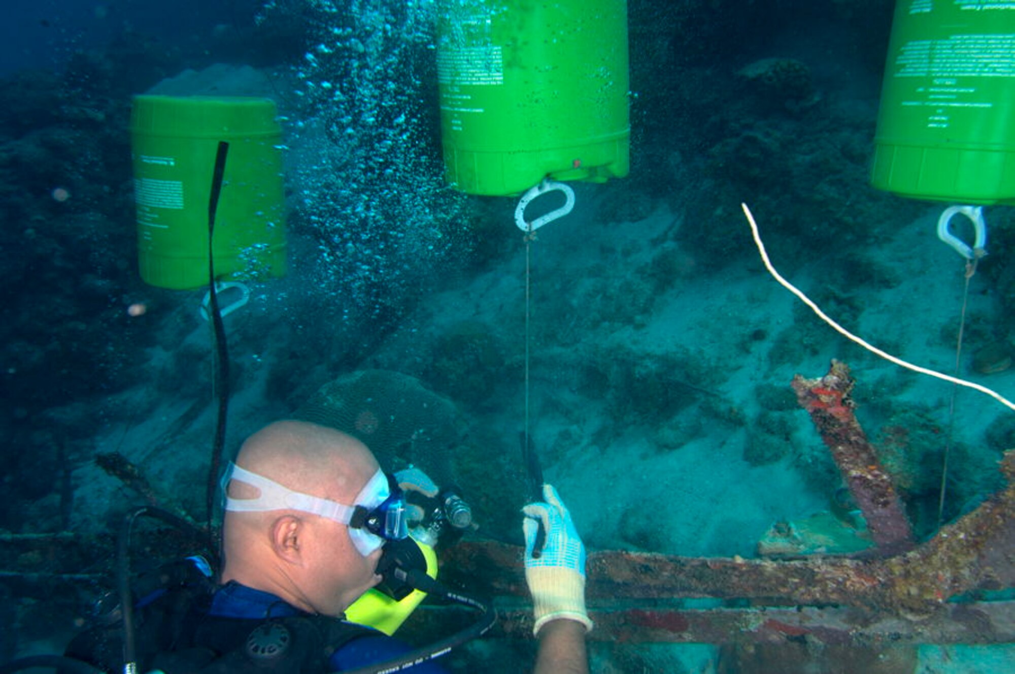 A scuba diver attaches several lifting drums to a deck railing on the Piscadera Beach coral reef to prepare it to be lifted to the surface.  Five gallon plastic drums were strategically placed around the coral reef clean-up area and once they were filled with air from the scuba diver’s tanks they floated to the surface and were collected for disposal.  After four coral reef clean-ups they have removed over 8,000 pounds of debris from the reef.  