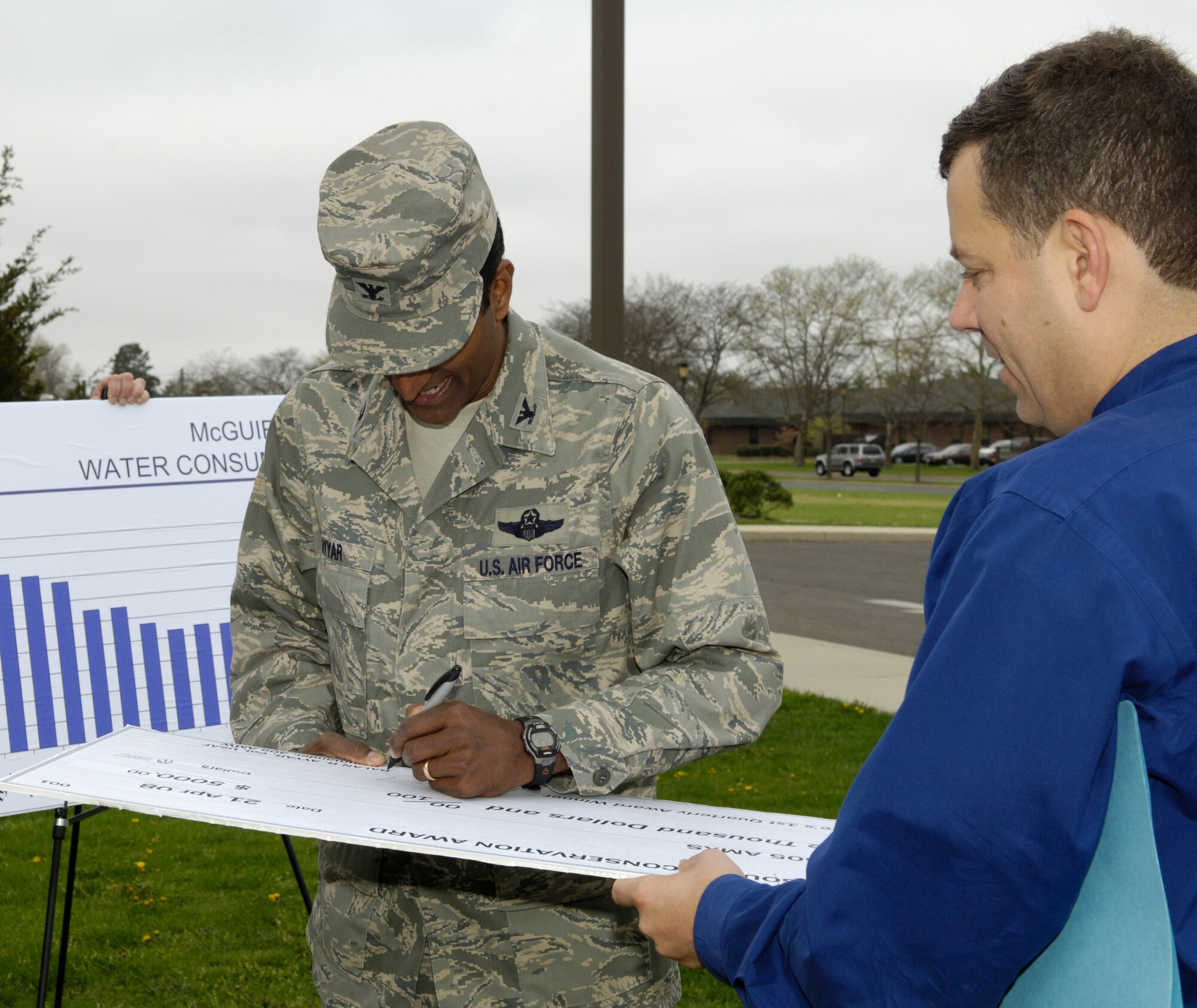 Col. Balan Ayyar, 305th Air Mobility Wing commander, presents a check to Lt. Col. Donald Atkinson, 605th Aircraft Maintenance Squadron commander, for winning the Resource Conservation Award during the Earth Week kick-off April 21 here. The squadron won the award for major reductions in its HAZMAT footprint and other environmental savings. Several activities are planned to celebrate Earth Week, including planting trees April 24 and a recycling drive in base housing April 25. (U.S. Air Force photo/Kenn Mann)