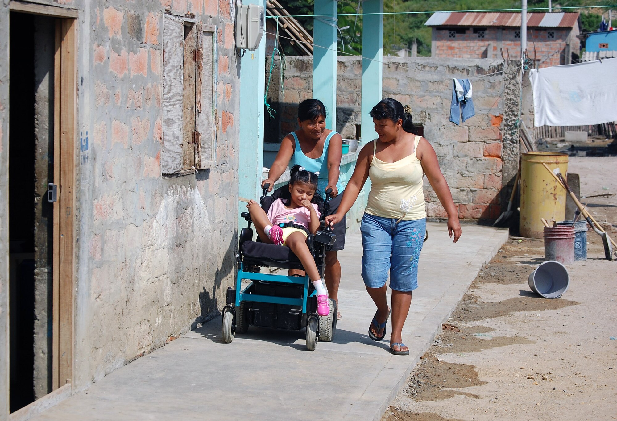 Eleven-year-old Kelly Yuleisy Arcentales is escorted by her mother (right) and aunt (left) on the new sidewalk that was paid for by donations collected by Airmen from the 964th Expeditionary Airborne Air Control Squadron who are deployed to Forward Operating Location Manta, Ecuador. The completion of the wheelchair ramp from Kelly's home to the Jaramijo city sidewalk finalized a three month project by the Airmen to provide Kelly with access to her local community. (U.S. Air Force photo/Capt. Ashley Norris) 
