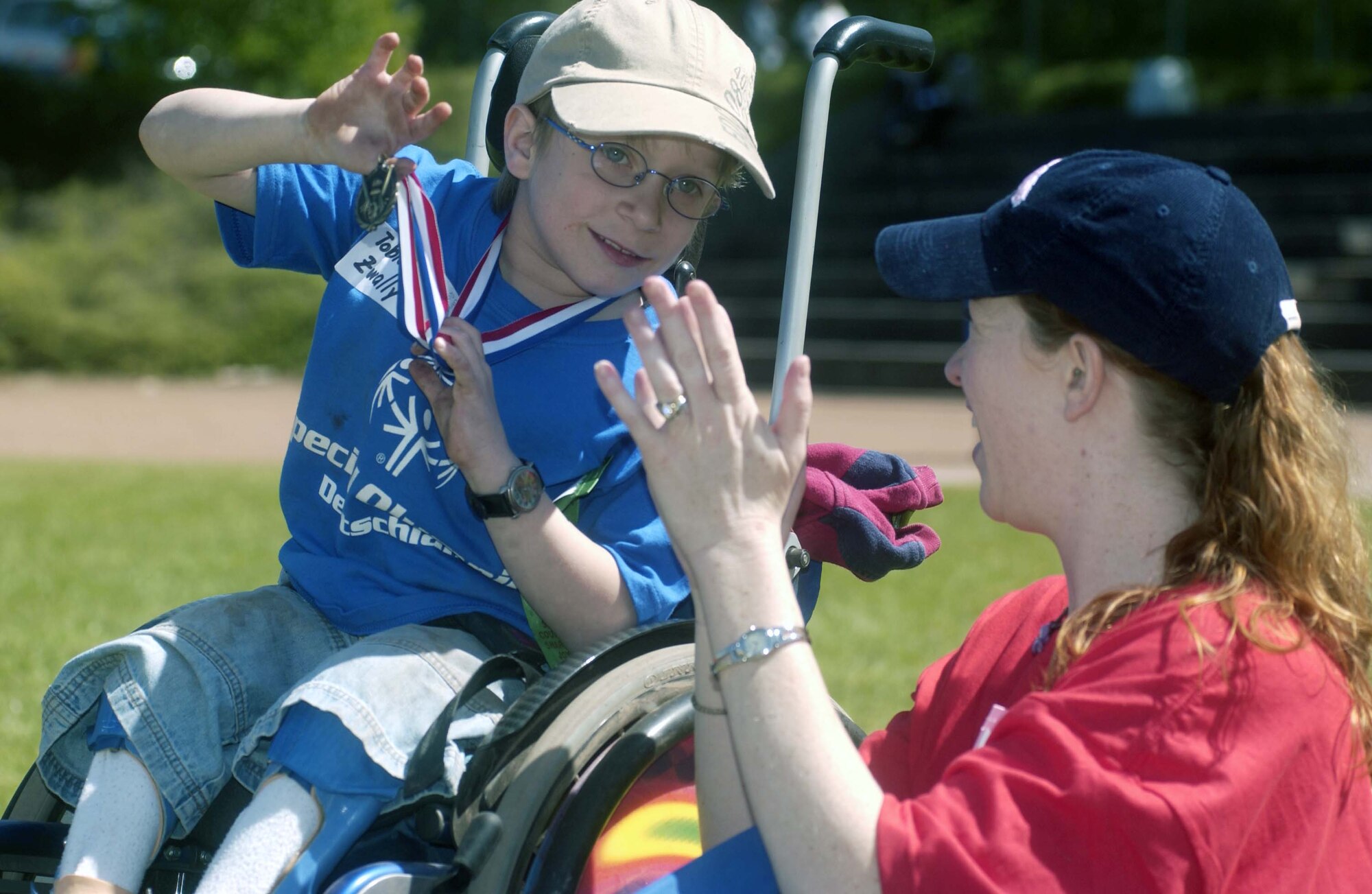 Tobias Zwally, 8, from the Reha-Westpfalz Schule in Landstuhl, Germany, shows his medal to his Buddy, Caryn Rodriguez, Vogelweh Elementary School fifth-grade teacher, while watching an exhibition soccer game between teams U.S.A. and Germany at the 2007 U.S. Army Garrison Kaiserslautern’s Special Olympics Spring Games at the Police Academy in Enkenbach-Alsenborn. Photo by Christine June 
