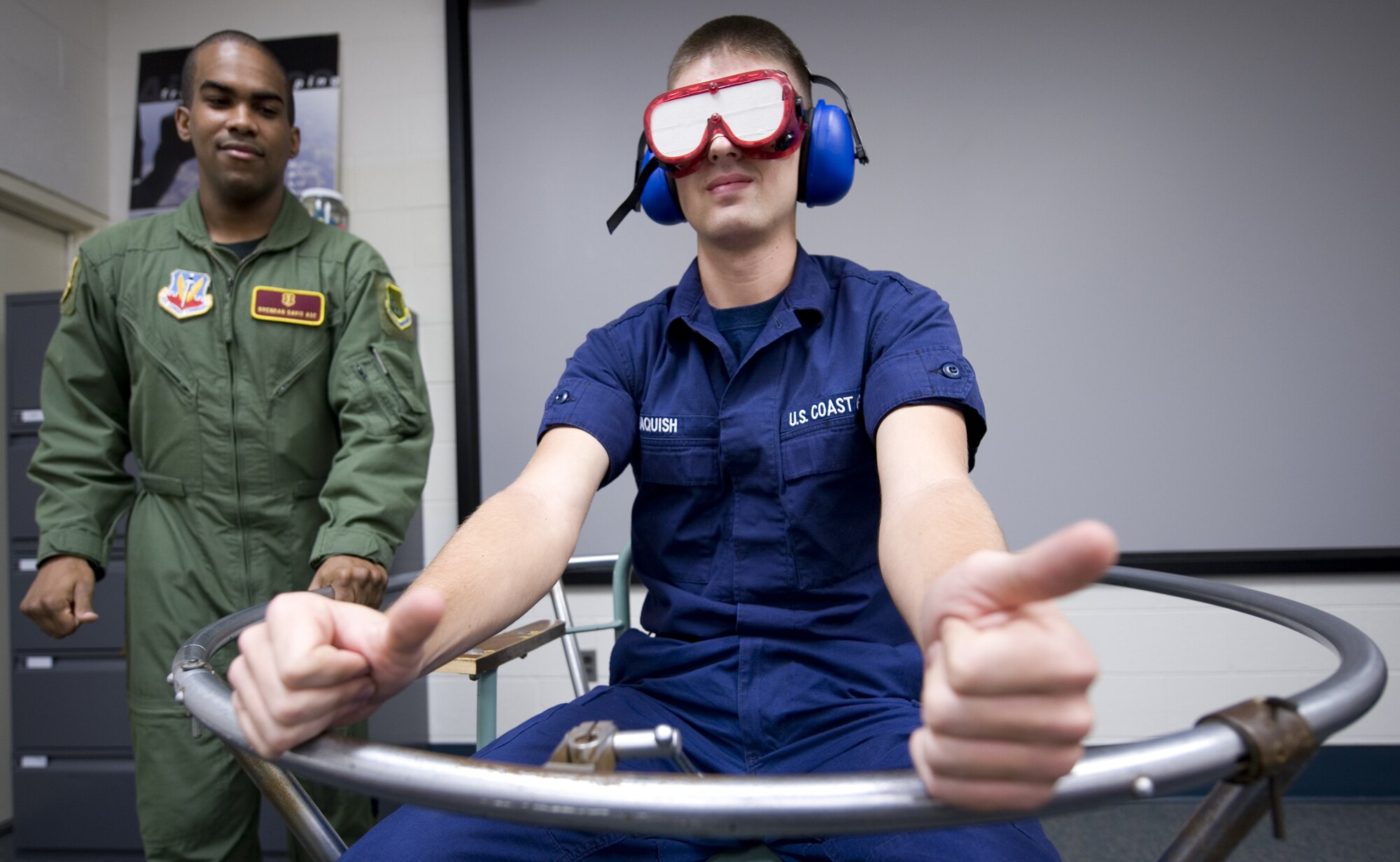 LANGLEY AIR FORCE BASE, Va. -- Airman 1st Class Brendan Davis (left), an Aerospace Physiology Apprentice with the 1st Aerospace Medicine Squadron, takes Airman Paul Jaquish, a United States Coast Guard Aviation Maintenance Technician student from Elizabeth City, N.C., Coast Guard Station, through a coriolis illusion exercise. Allowing him to feel the overwhelming illusion of change in direction while going through a prolonged turn during Altitude Chamber Training on March 23. (U.S. Air Force Photo/Staff Sgt. Samuel Rogers)