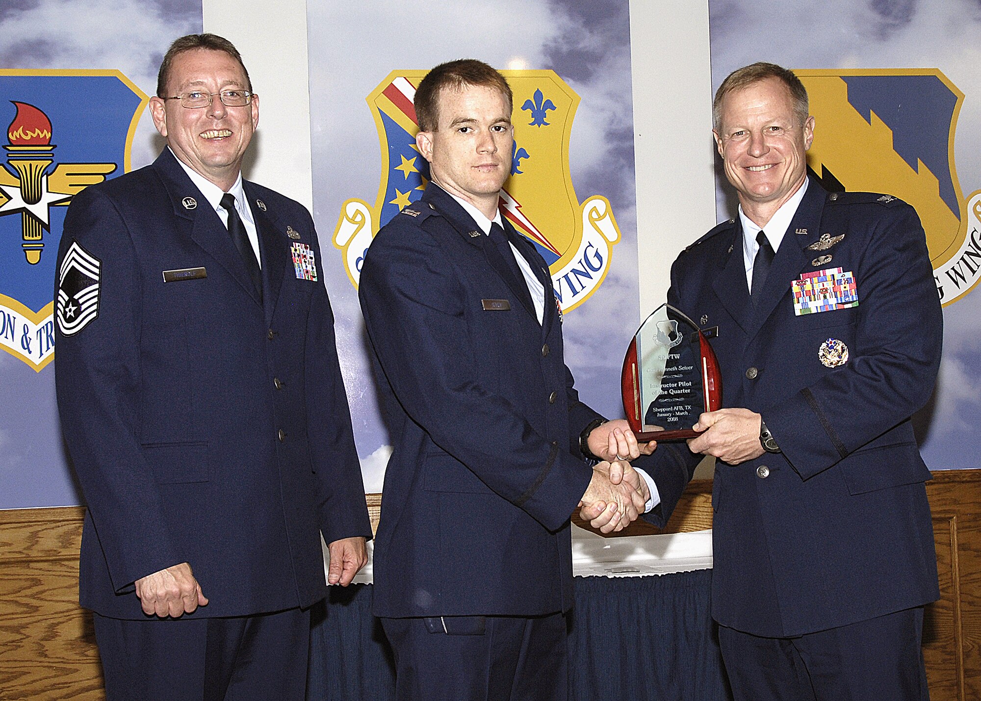 Capt. Kenneth Siever, 88th Fighter Training Squadron, accepts the Instructor Pilot of the Quarter award from 80th Flying Training Wing Commander Col. David Petersen April 22 during the wing's quarterly award ceremony. Captain Siever was recognized for having a 100 percent graduation rate in the Introduction to Fighter Fundamentals course. He is also working on a Masters of Business Administration degree. Also pictured is 80th FTW Superintendent Chief Master Sgt. Norman Theirolf. (U.S. Air Force photos/Harry Tonemah)