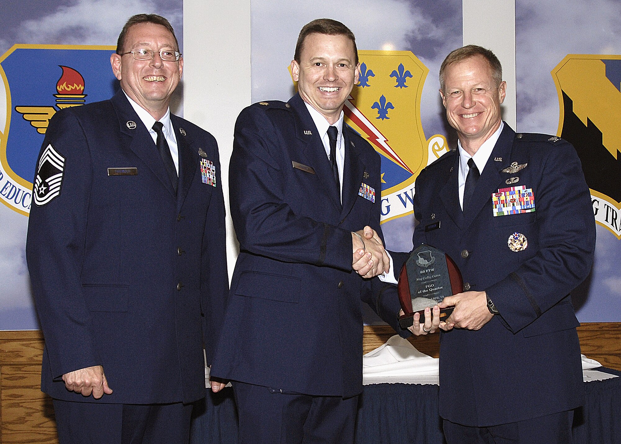 Maj. Colby Cates accepts the Field Grade Officer of the Quarter award from Col. David Petersen, commander of the 80th Flying Training Wing, April 22 at the wing's quarterly award luncheon. Major Cates was recognized for his efforts with the incoming T-6A Texan IIs, pursuing a masters degree through Air University and being involved in his church and coaching T-Ball in the Wichita Falls Little League. Also pictured is 80th FTW Superintendant Chief Master Sgt. Norman Thierolf. (U.S. Air Force photo/Harry Tonemah)