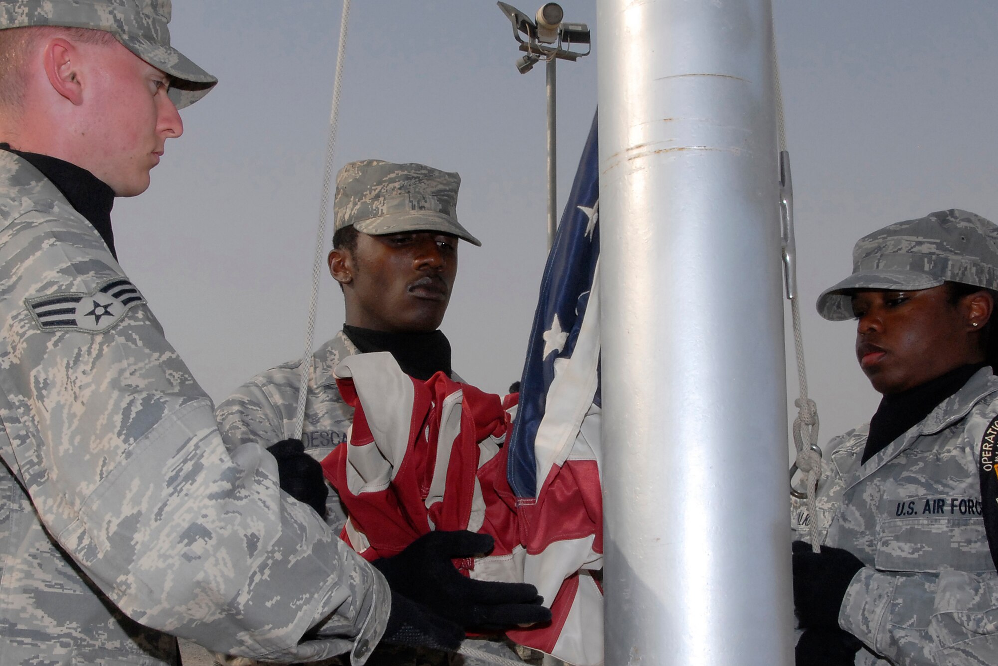 SOUTHWEST ASIA – Honor guardsman Airman 1st Class JoVan Descartes, (center), embraces the American flag during the 386th Expeditionary Mission Support Group retreat ceremony held at an air base in the Persian Gulf Region April 25, 2008. Senior Airman Rian Hudson, in the fold-position and Senior Airman Tausha Walker, in the hold-position, stoically lower the flag during the expedited retreat ceremony. (U.S. Air Force photo/Tech. Sgt. Michael O’Connor)