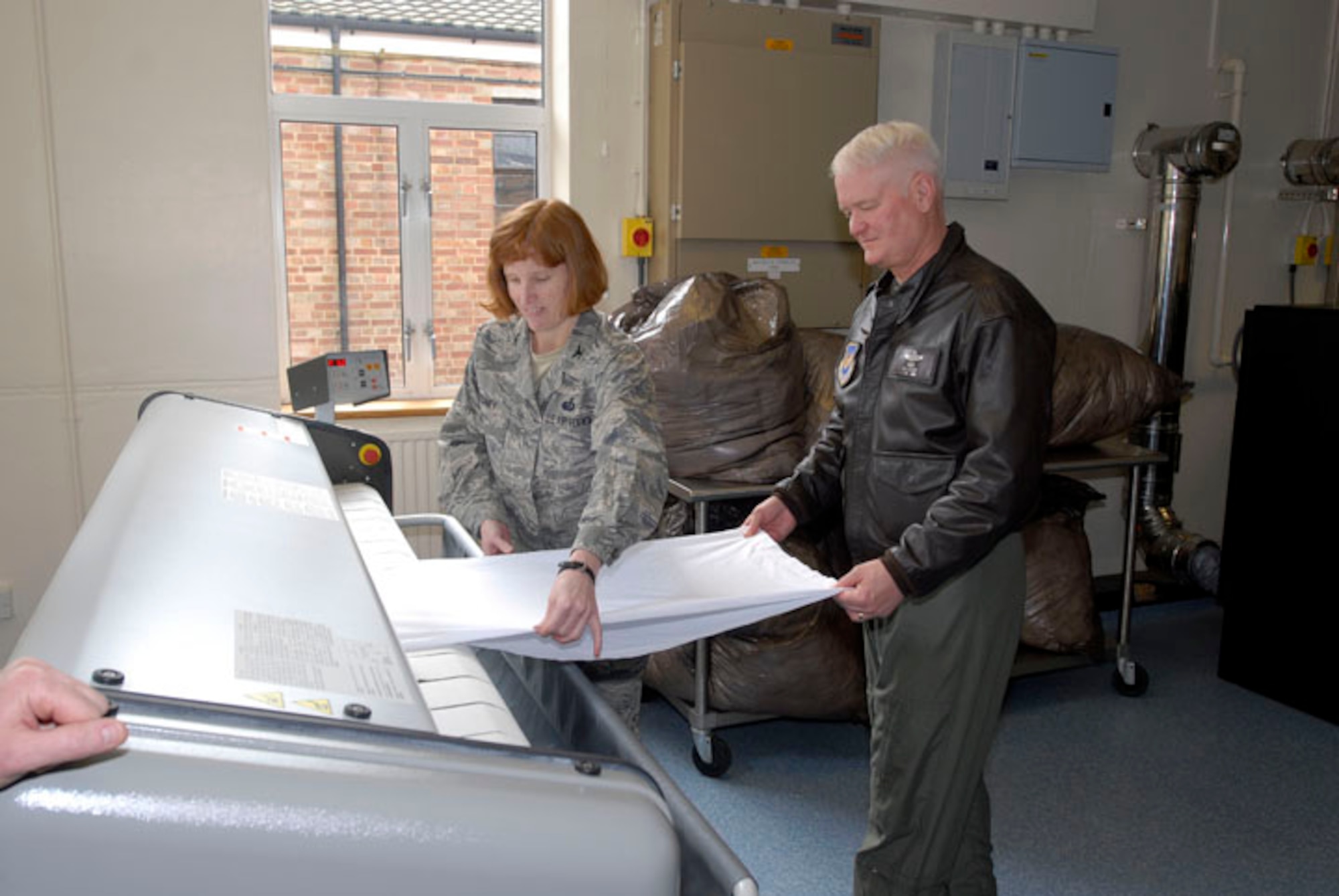 Lt. Gen. Rod Bishop, Third Air Force commander, and Col. Kimbery Toney, 501st Combat Support Wing commander learn to use a "flat press ironer"  as part of a new project for th 420th Air Base Squadron Services flight at RAF Fairford.  Mr. Larry Krauss, Chief of Services, said the Air Force had to pay for this laundry service, which was very costly. He decided they could do it in-house and save money. The project worked so well, they took on laundry services at RAF Croughton as well. (U.S. Air Force Photo by Senior Master Sgt. John Nicolussi)