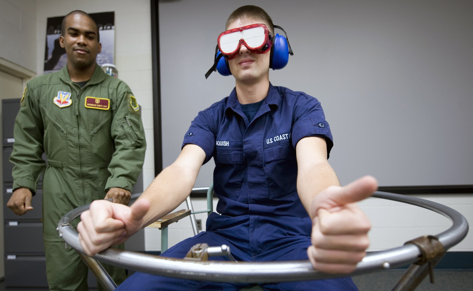 Airman 1st Class Brendan Davis (left) takes Airman Paul Jaquish through a spatial disorientation exercise March 23 at Langley Air Force Base, Va. A spinning device, called a Barany Chair, is used to simulate aircraft maneuvers using centrifugal force. The chair produces disorientation similar to what pilots commonly experienced during flight maneuvers. Airman Davis is an aerospace physiology apprentice with the 1st Aerospace Medicine Squadron and Airman Jaquish is a Coast Guard aviation maintenance technician student from Elizabeth City, N.C., Coast Guard Station. (U.S. Air Force Photo/Staff Sgt. Samuel Rogers) 