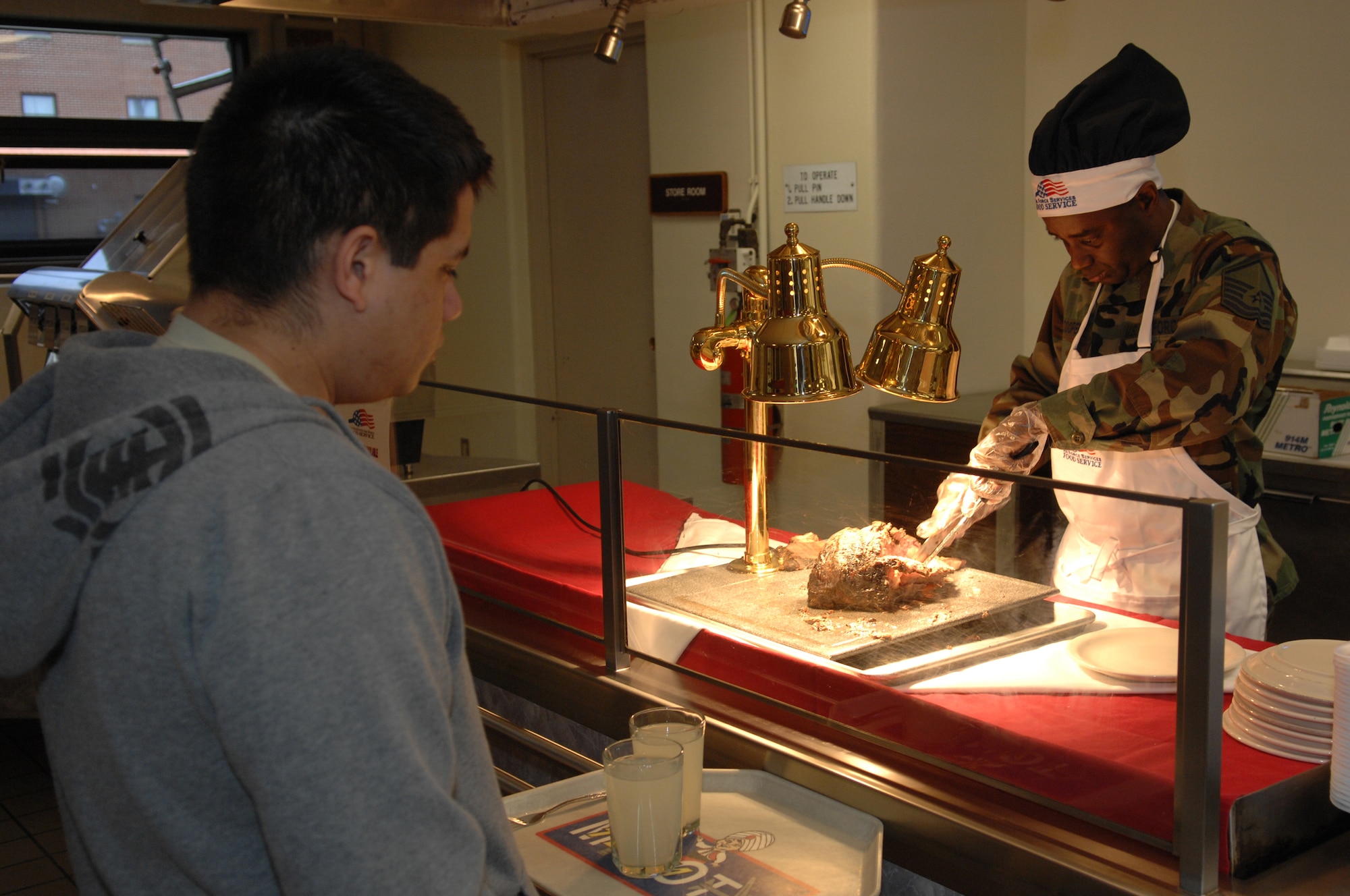 MINOT AIR FORCE BASE, N.D. —  Master Sgt. Anthony Cooper, 5th Operations Group functional manager, cuts Airman 1st Class John Guerrero, 5th Munitions Squadron storage crew member, a piece of meat during the Airmen Appreciation Meal at the Dakota Inn Dining Facility April 24. Sergeant Cooper, along with group commanders, first sergeants and chiefs, volunteered to serve Airmen dinner at the DFAC to show their appreciation for the service and dedication of junior Airmen. (U.S. Air Force photo by Senior Airman Cassandra Jones)