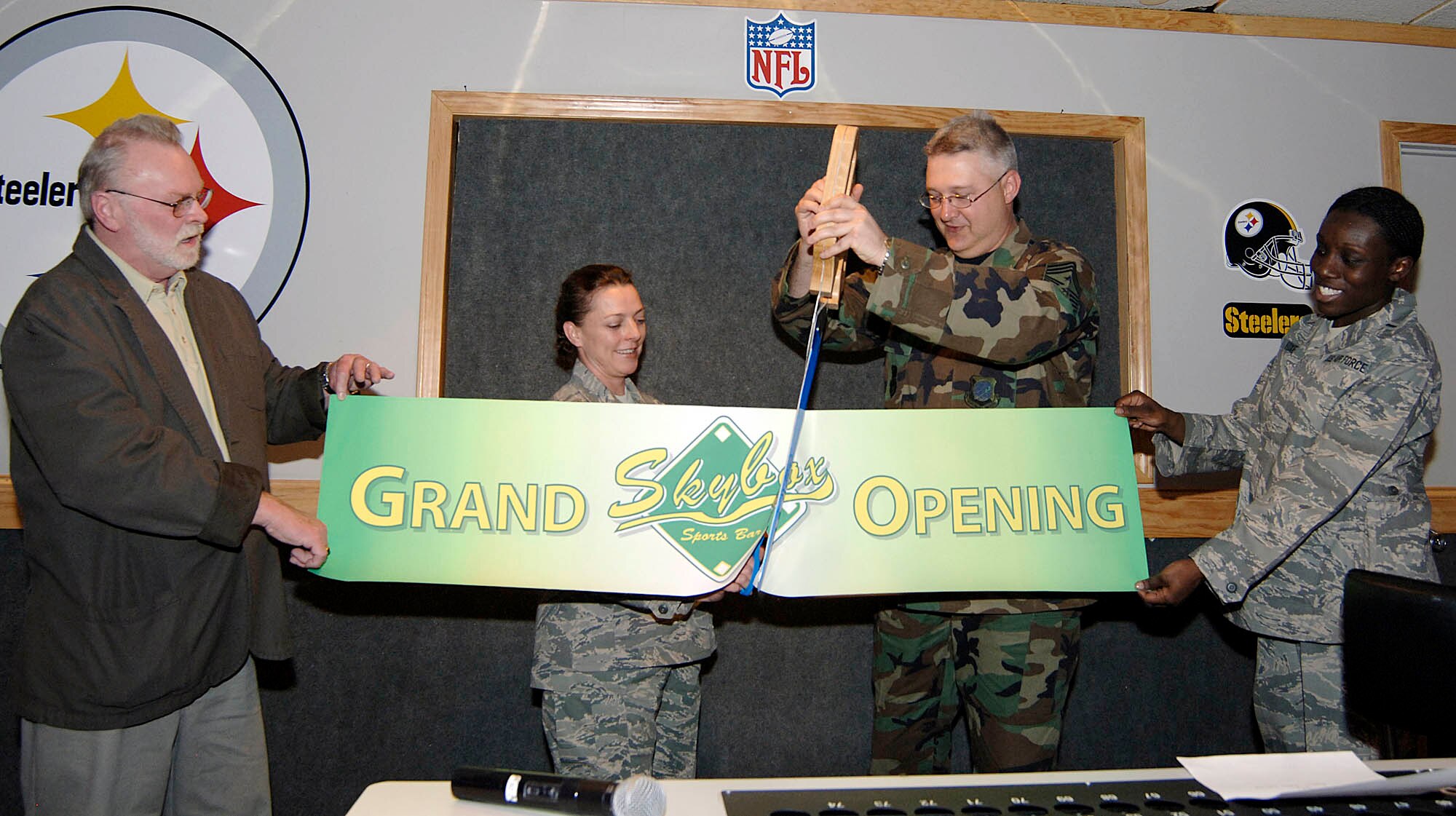 FAIRCHILD AIR FORCE BASE, Wash. – Terry Bozman, 92nd Services Squadron community support flight chief, and 1st Lt. Lenora Foxe, 92nd Services Squadron deputy flight chief, hold the banner while Chief Master Sgt. Paul Sikora, 92nd Air Refueling Wing command chief, and Senior Master Sgt. Crystal White, 92nd Services Squadron combat support flight superintendent, cut a banner honoring the grand opening of the newly remodeled enlisted club April 25. The club has added flat-panel televisions, sports memorabilia and posters supporting the sports bar theme. It also received a new name with the grand opening SkyBox replaces the old name of Hollywood North. (U.S. Air Force photo / Staff Sgt. JT May III)