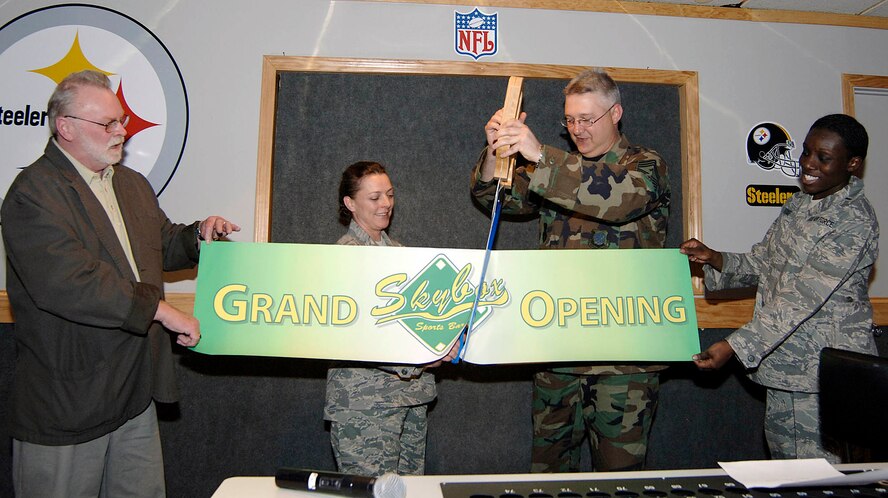 FAIRCHILD AIR FORCE BASE, Wash. – Terry Bozman, 92nd Services Squadron community support flight chief, and 1st Lt. Lenora Foxe, 92nd Services Squadron deputy flight chief, hold the banner while Chief Master Sgt. Paul Sikora, 92nd Air Refueling Wing command chief, and Senior Master Sgt. Crystal White, 92nd Services Squadron combat support flight superintendent, cut a banner honoring the grand opening of the newly remodeled enlisted club April 25. The club has added flat-panel televisions, sports memorabilia and posters supporting the sports bar theme. It also received a new name with the grand opening SkyBox replaces the old name of Hollywood North. (U.S. Air Force photo / Staff Sgt. JT May III)
