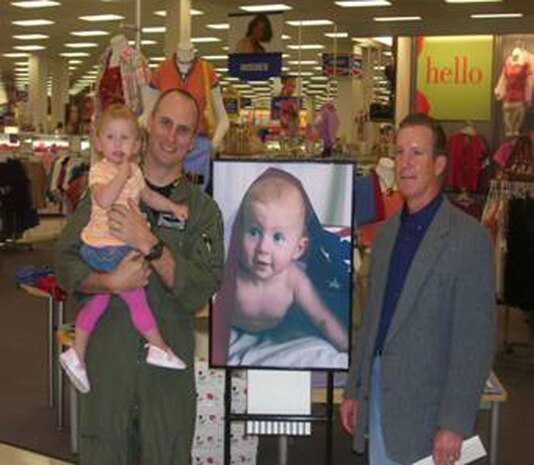 NELLIS AIR FORCE BASE, Nev. -- Kenneth Klein, Nellis Base Exchange general manager, presented Maj. Brett Waring, 66th Weapons Squadron weapons instructor pilot, with a $2,500 check April 17 for winning second place in the Army and Air Force Exchange Service’s “Picture This” Pog Design Contest. Major Waring's pog design, featuring his daughter Addison Claire, will be used instead of actual coins at AAFES establishments in the U.S. Central Command Area of Responsibility. (courtesy photo)