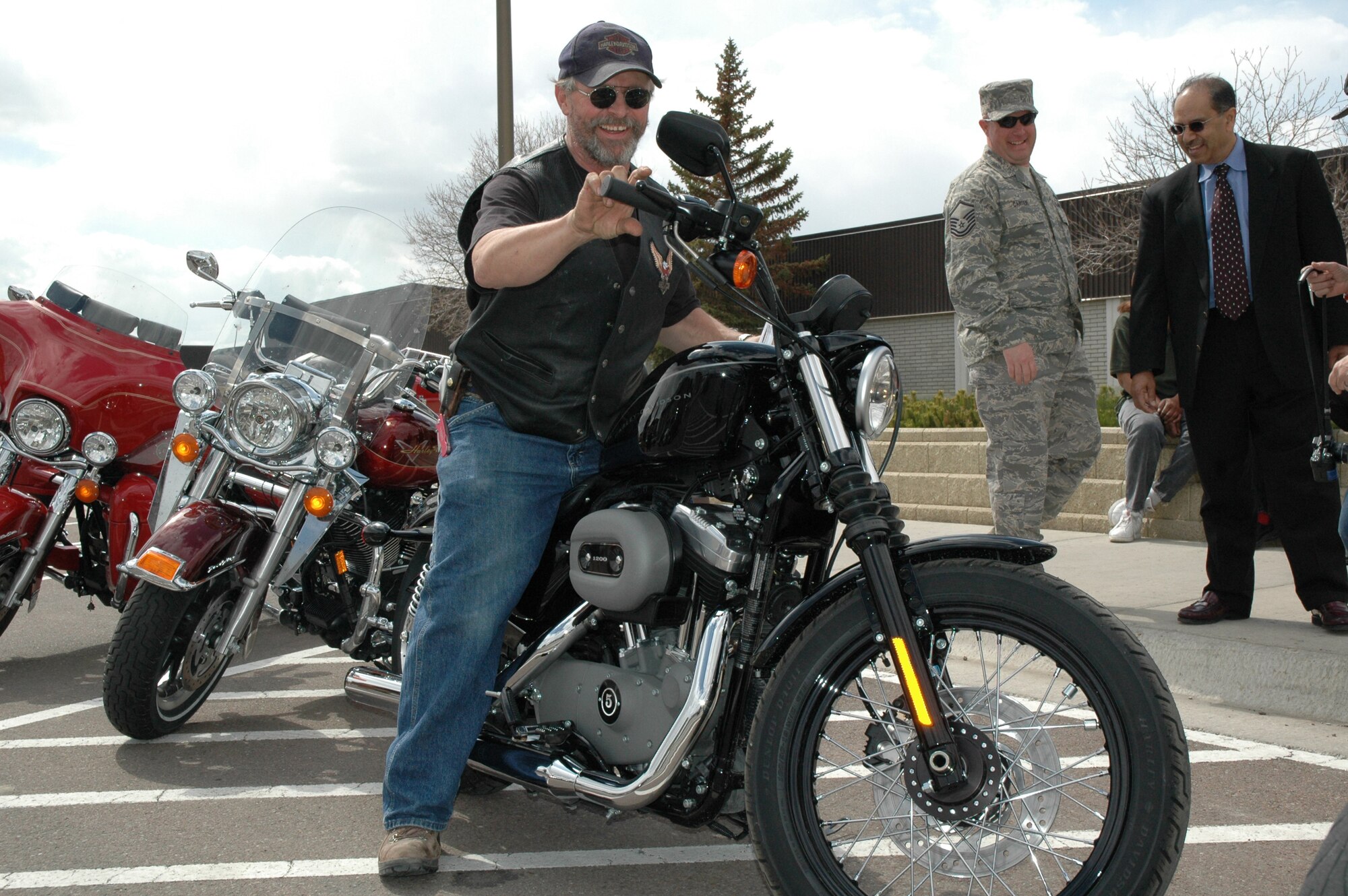 Retired Master Sgt. Ted Baker hops on his new Harley 1200 Sportster outside the Base Exchange April 28, as Master Sgt. Kevin Carter, 341st Civil Engineer Squadron, and Russell Mendoza, district sales manager of Sandberg and Sikorski, look on. He had just learned he was the winner of an AAFES-wide sweepstakes. Sandberg and Sikorski is a New York based company that supplies jewelry to AAFES. The company sponsored the sweepstakes and Mr. Mendoza came to Malmstrom to present Mr. Baker his prize. (U.S. Air Force photo/Airman 1st Class Emerald Ralston)