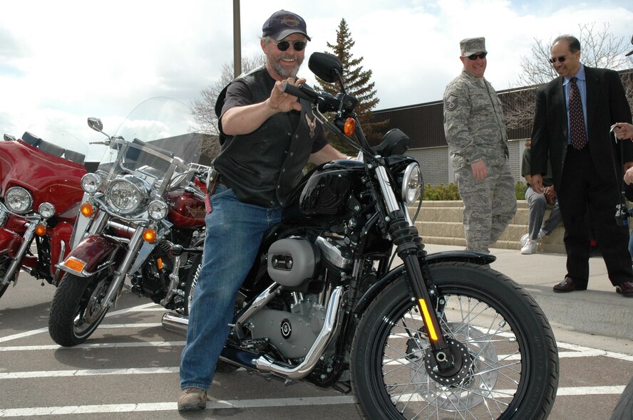 Retired Master Sgt. Ted Baker hops on his new Harley 1200 Sportster outside the Base Exchange April 28, as Master Sgt. Kevin Carter, 341st Civil Engineer Squadron, and Russell Mendoza, district sales manager of Sandberg and Sikorski, look on. He had just learned he was the winner of an AAFES-wide sweepstakes. Sandberg and Sikorski is a New York based company that supplies jewelry to AAFES. The company sponsored the sweepstakes and Mr. Mendoza came to Malmstrom to present Mr. Baker his prize. (U.S. Air Force photo/Airman 1st Class Emerald Ralston)