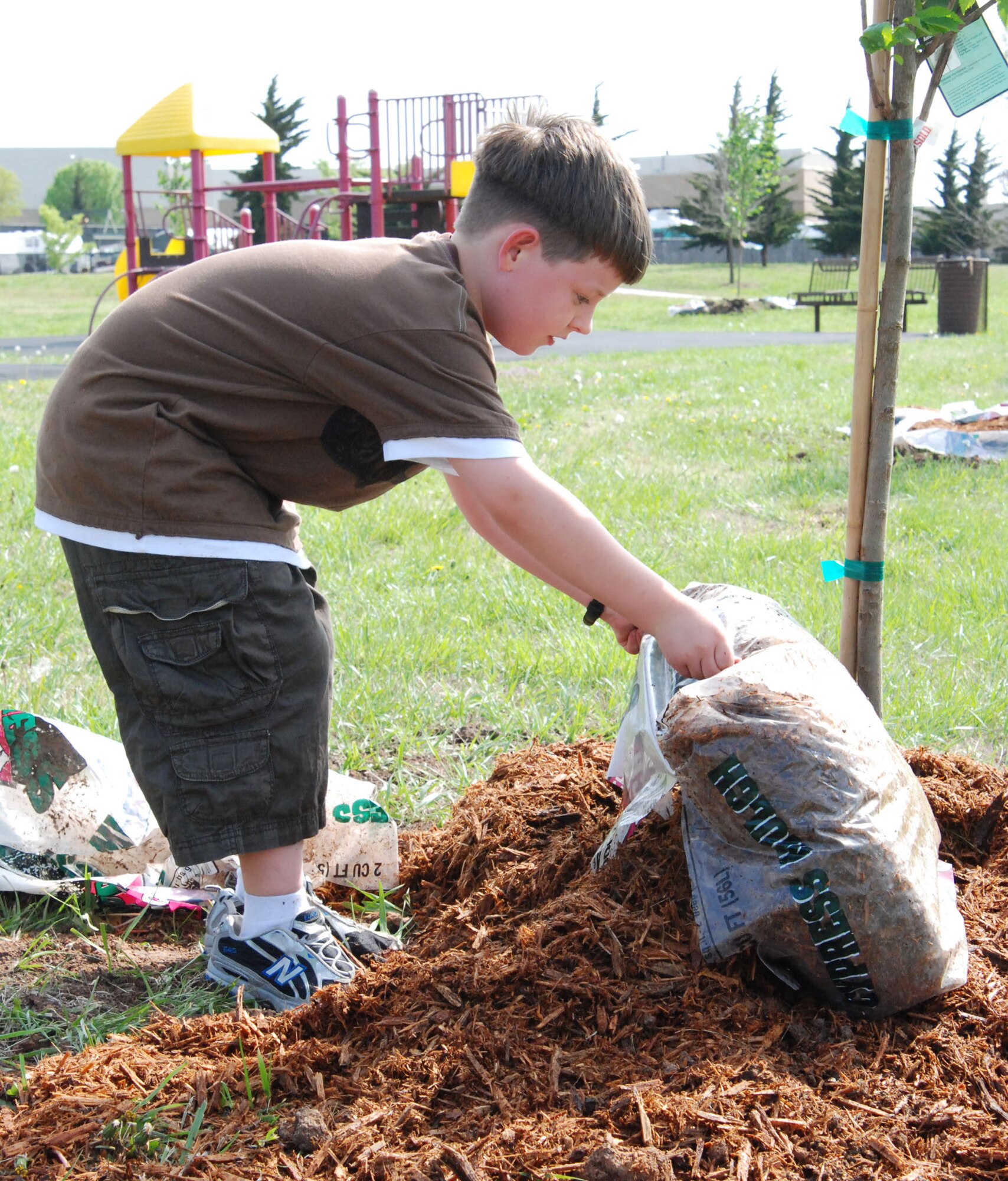 MCCONNELL AIR FORCE BASE, Kan. – Peter Fischer, Team McConnell youth, dumps a bag of mulch over a newly planted tree at an Arbor Day Ceremony, April 24. Base and local community children from Oaklawn Elementary School helped plant 12 new trees on base. (photo by Airman 1st Class Jessica Lockoski)  