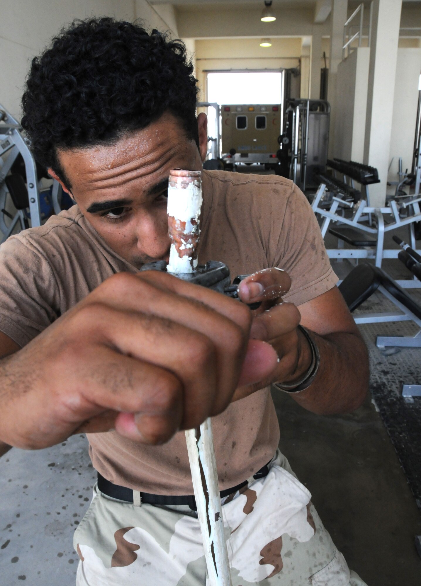 SOUTHWEST ASIA -- Airman Judah Trimmer, 379th Expeditionary Civil Engineer Squadron utilities systems journeyman, from Minot Air Force Base, N.D., uses a pipe cutter to remove a section of damaged water pipe at fire station No. 2 April 26. The removed section was rubbing against the bracket holding the pipe to the wall, causing it to leak. (U.S. Air Force photo/ Senior Airman Tong Duong.)