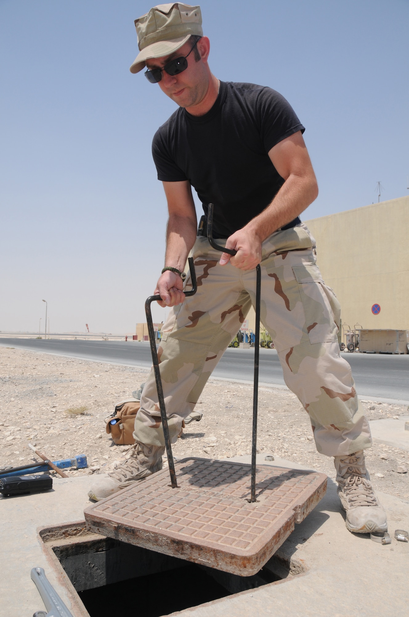 SOUTHWEST ASIA-- Staff Sgt. Daron Tienhaara, 379th ECES utilities systems
journeyman, uses a puller to open a manhole cover outside fire station No. 2
April 26. He is attempting to isolate a water main valve to cut off water to a leaking
pipe.  (U.S. Air Force photo/ Senior Airman Tong Duong.)