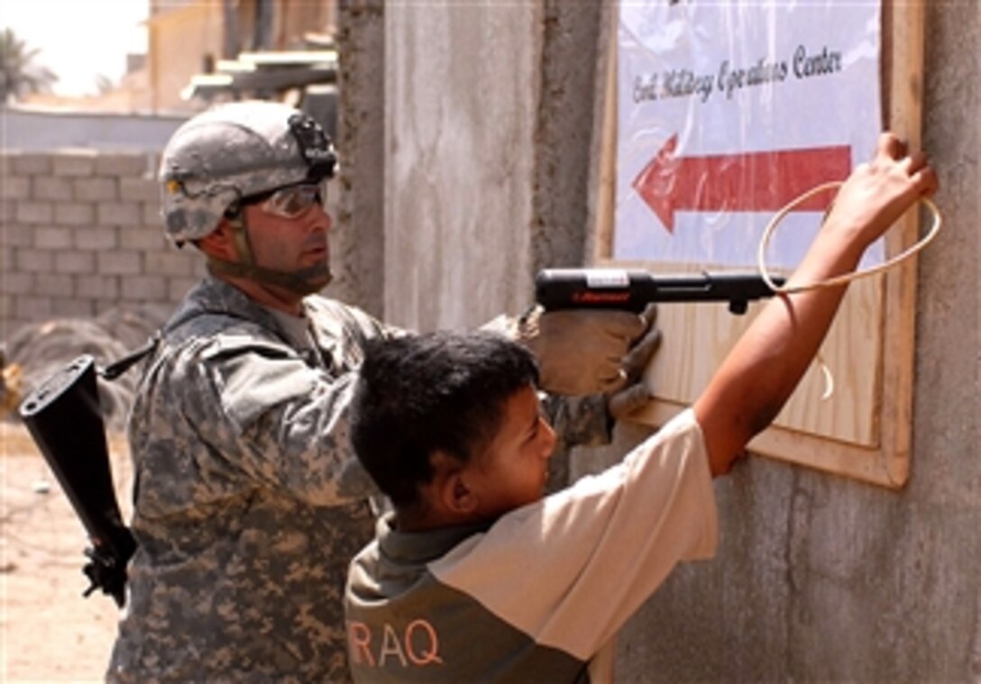 U.S. Army Staff Sgt. Robert Groves nails a sign in place as an Iraqi boy holds it, April 27, 2008. The sign instructs visitors to the newly opened Civil Military Operations Center on Joint Security Station Sadr City. Groves is assigned to the 4th Infantry Division's 3rd Brigade Combat Team.

