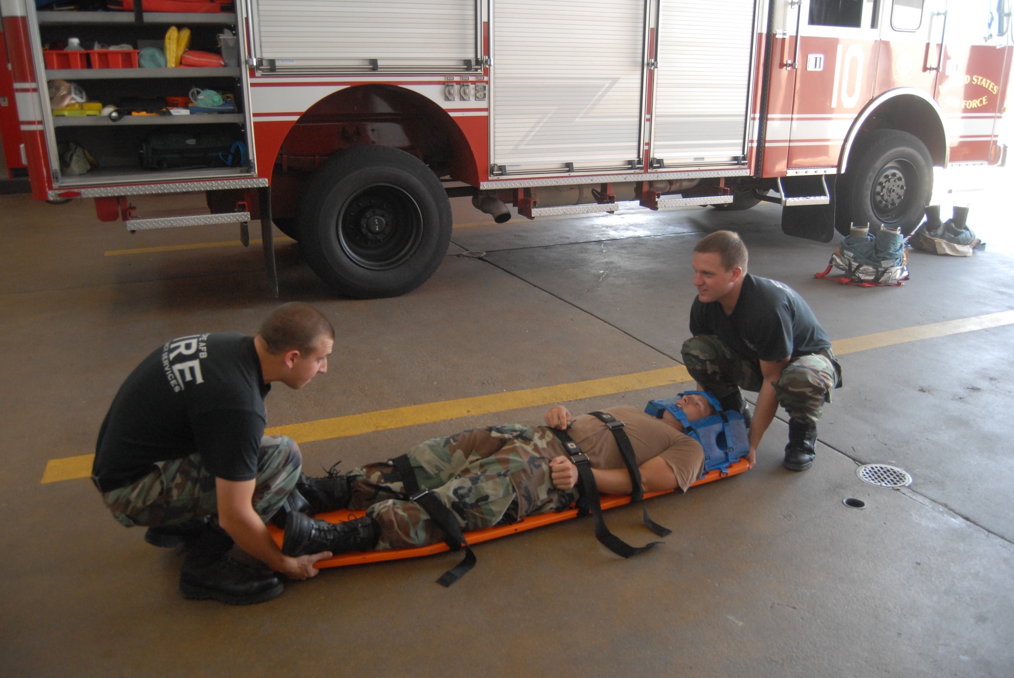Airmen 1st Class Devon Wildes and Kyle Schmidt carry Airman 1st Class Daniel Norris on a stretcher as part of self-aid buddy care demonstration July 28. This exercise simulates a neck or spinal injury that leaves a victim completely immobilized. This training exercise is one of many that Pope firefighters must rehearse on a frequent basis. (U.S. Air Force Photo by Emily Smith)