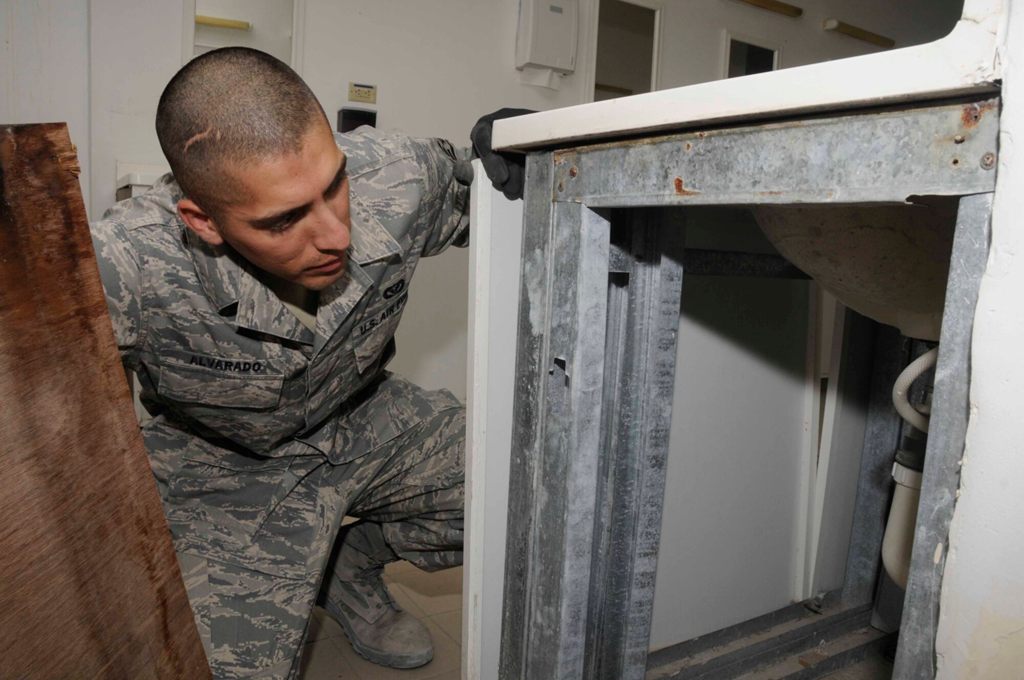 Staff Sgt. Cesar Alvarado, 379th Expeditionary Civil Engineer Squadron, removes plywood to check for water damage behind the cadillac sinks July 30 in Southwest Asia. Cadillacs are bathroom facilities for deployed military members and its Sergeant Alvarado’s job to perform daily maintenance on it. Sergeant Alvarado is a structural journeyman deployed from Eglin Air Force Base, Fla. (U.S. Photo/Staff Sgt. Darnell T. Cannady)