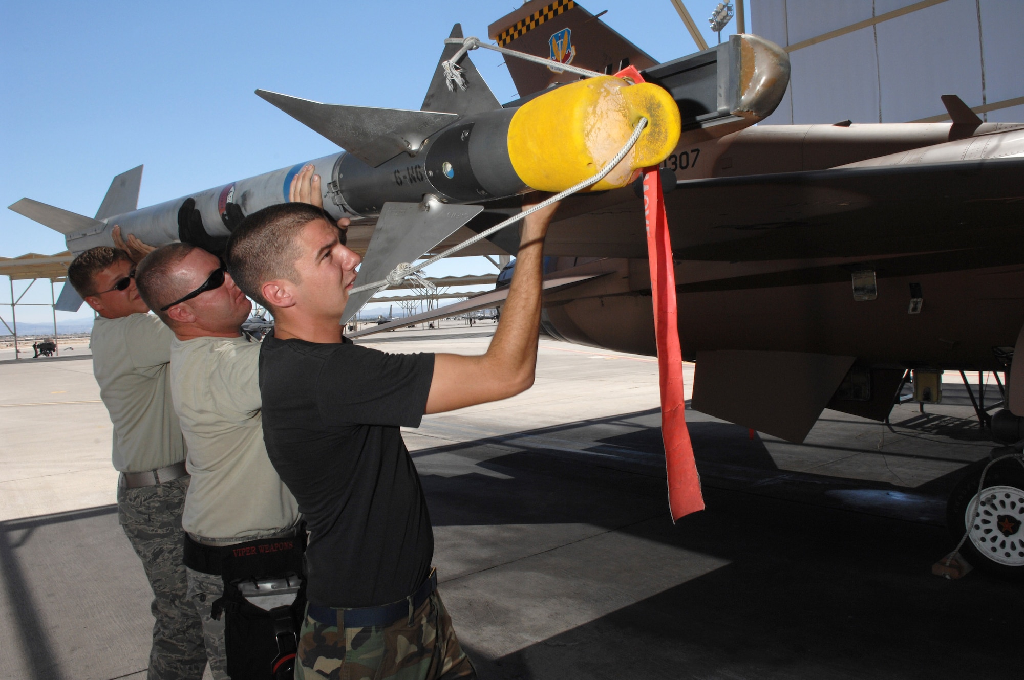 Senior Airman Gregory Strouse (left to right), Staff Sgt. Sean Minnick and Senior Airman David Garrison load a missile onto a F-16 Fighting Falcon July 24 at Nellis Air Force Base, Nev. The 926th Group is an Air Force Reserve unit under the 10th Air Force, Naval Air Station Joint Reserve Base, Fort Worth, Texas. The group is located at Nellis AFB as an associate unit to the Air Force Warfare Center. Through total force integration, reservists are integrated into active duty Air Force units, accomplishing the mission alongside active-duty Airmen on a daily basis. Airman Strouse is a 57th Aircraft Maintenance Squadron F-16 weapons load crew member, Sergeant Minnick is a 926th Group Det. 2 F-16 weapons loader team chief, and Airman Garrison is a 57th AMXS F-16 weapons load crew member. (U.S. Air Force photo/Senior Airman Larry E. Reid Jr.)
