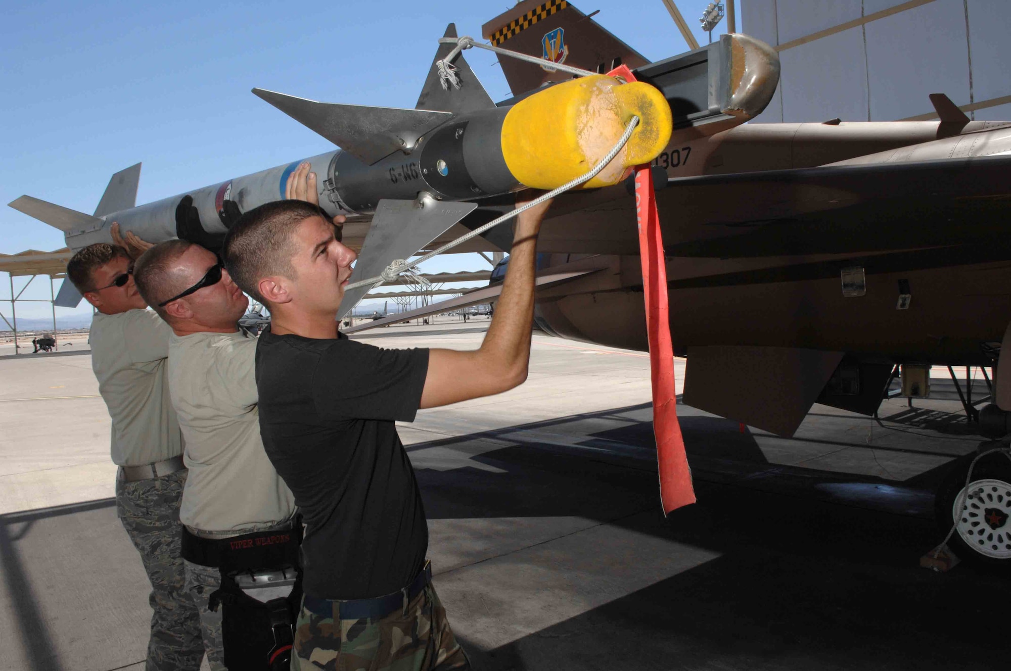 Senior Airman Gregory Strouse (left), 57th Aircraft Maintenance Squadron F-16 weapons load crew member; Staff Sgt. Sean Minnick (center), 926th Group Detachment 2 F-16 weapons loader team chief; and Senior Airman David Garrison, 57th AMXS F-16 weapons load crew member, load a missile onto an F-16 July 24, 2008, at Nellis Air Force Base, Nev. (U.S. Air Force photo/Senior Airman Larry E. Reid Jr.)