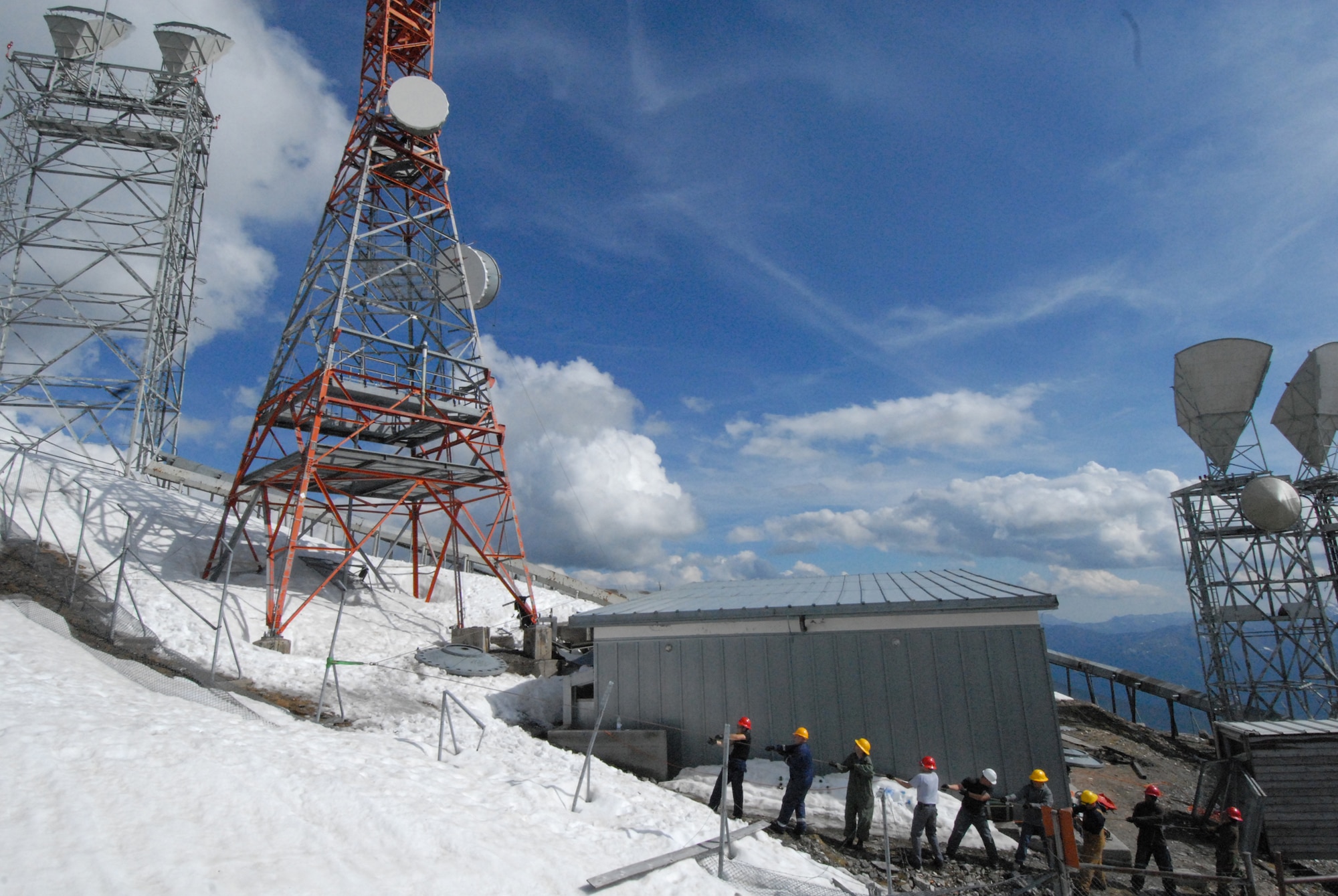 Senior Airman Carlos Salinas, Master Sgt. Eric Kastner, Tech. Sgt. Shannon Meredeth, Maj. Mike Phillips, Senior Airman Jason Cecala, Senior Airman Rudy Mendez, Staff Sgt. Jered Smither, Tech Sgt. Terrance Drayton and Senior Airman Mayra Christian, all assigned to the 1st Communications Maintenance Squadron work together to lower a dish in the snow atop Cima Galina, Italy. (Courtsey photo)