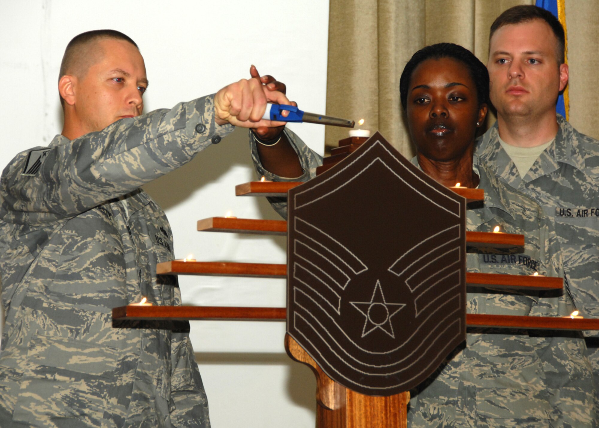SOUTHWEST ASIA -- Master Sgt. Roger Modesty, 386th Expeditionary Maintenance Squadron, and Tech. Sgt. Erica Buckner, 386th Expeditionary Logistics Readiness Squadron, light a candle together during the Senior Noncommisioned Officer Induction Ceremony Aug. 2 at a base in Southwest Asia. Each candle sitting on the insignia represented a step through the ranks each of the inductees had made to become senior NCOs.  