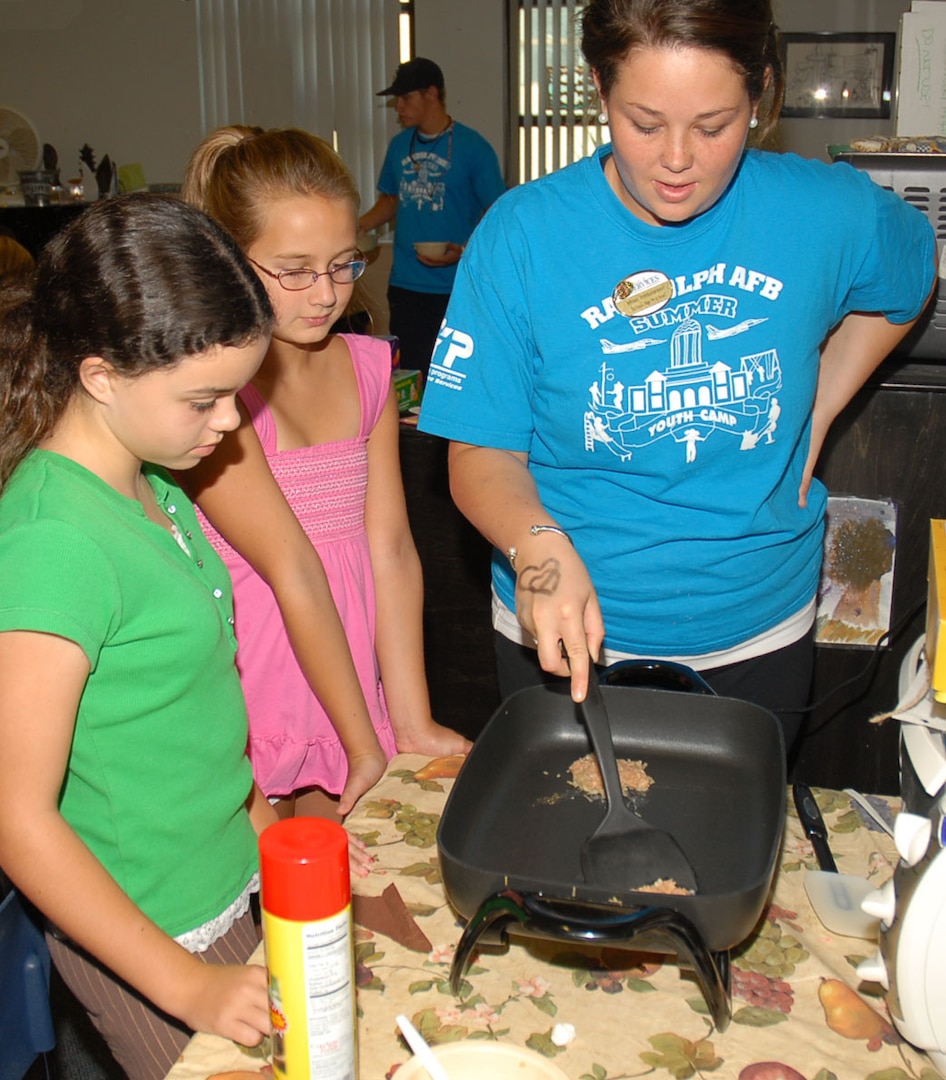 Allison Przybyslawski, a Texas A&M University student and school-age program assistant, helps flip a hashbrown for Tara Schwehm (left), 11, and Kylie Nugent, 9 during a cooking class at the Randolph Youth Center Aug. 6. (Photo by Thomas Warner)