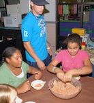 Tyler Betts, a Stephen F. Austin State University student and Randolph Youth Center school-age program assistant, supervises Cecilia Sunchild (left), 10, and Madi Beck, 11, make the batter for has browns during a cooking class Aug. 6 at the youth center. (Photo by Thomas Warner)