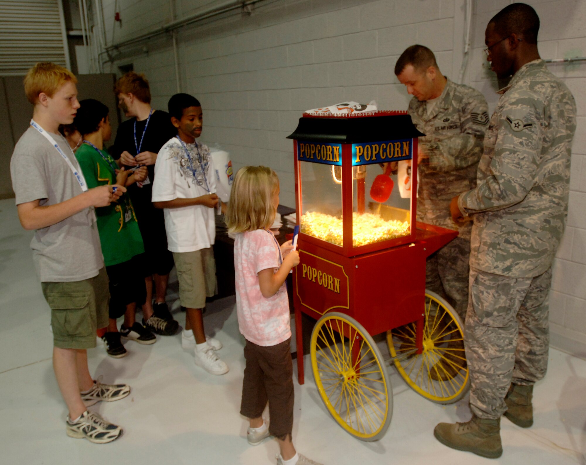 LANGLEY AIR FORCE BASE, Va. -- Tech. Sgt. Brian Brown, Air Force Combat Intelligence Surveillance Reconnaissance communications technician, and Airman Antwun Cotton, 735th Supply Chain Management Group mission capability technician, volunteer their time to serve popcorn to children at the Operation Hero event here on Aug. 24.  Operation Hero is a program to educate military children about deployments.  (U.S. Air Force photo/Tech. Sgt. Levi Collins) 