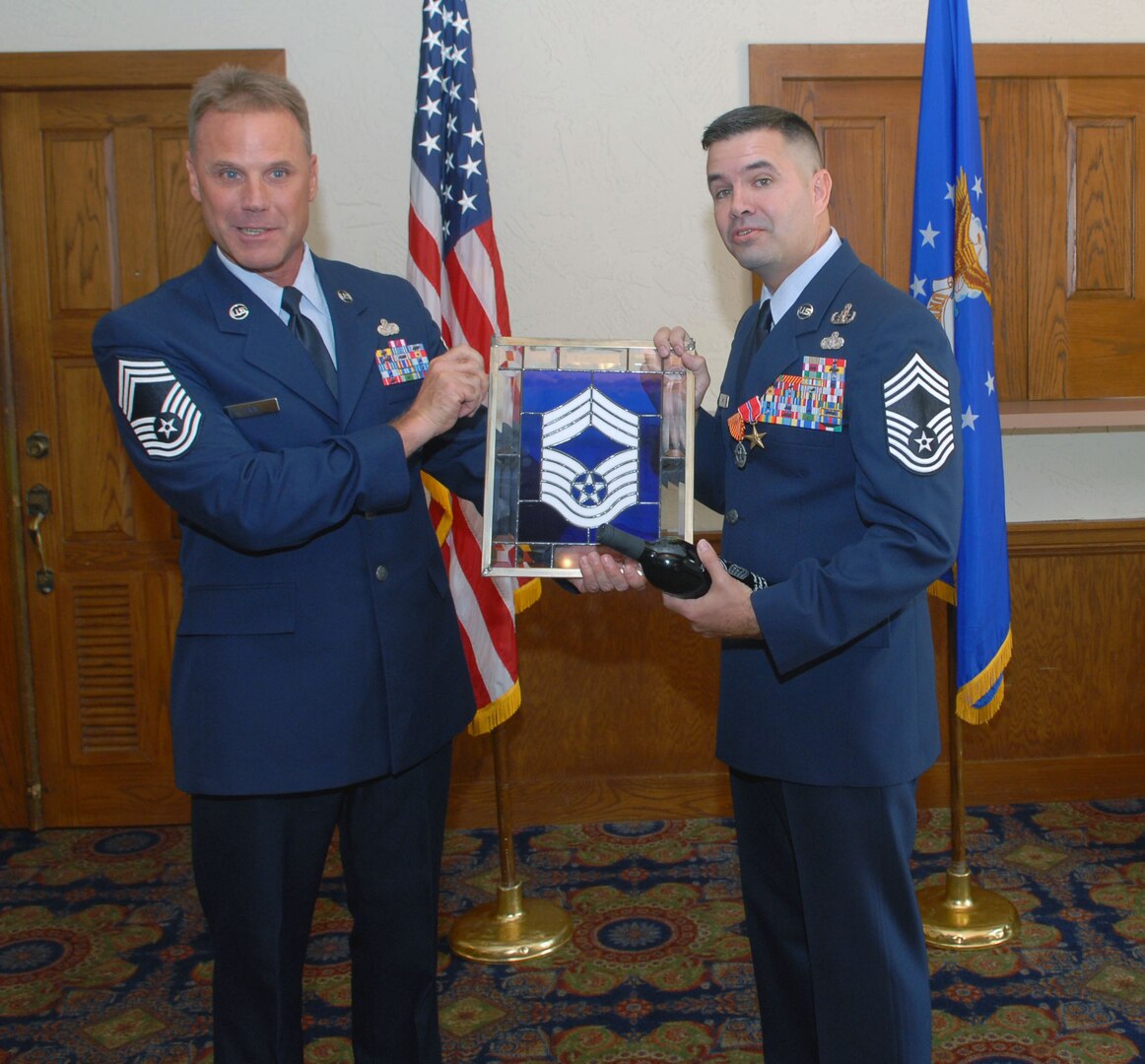 Chief Master Sgt. Joseph May Jr. (right), Air Education and Training Command's explosive ordnance disposal functional manager, accepts a stained glass chief master sergeant symbol from Chief Master Sgt. David Fain during a ceremony Aug. 1. During the ceremony, Chief May received a triple crown -- he was officially promoted to chief master sergeant and awarded his first Combat Action Medal and second Bronze Star. The stained glass, a gift from the Randolph Chief's Group, is traditionally presented to new chiefs. (U.S. Air Force photo by Rich McFadden)