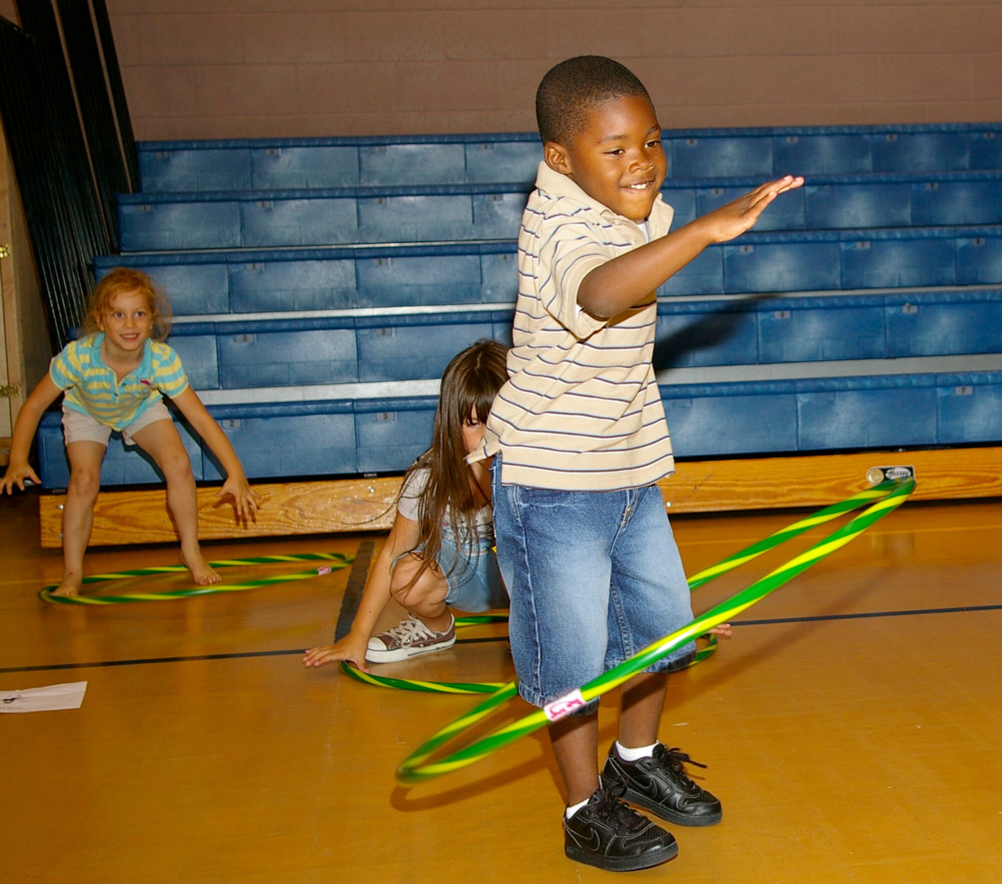 Joseph London, 5, 100th Communications Squadron family member, concentrates really hard as he does the hula hoop during a specially devised circuit class at the RAF Mildenhall Youth Center Aug. 1. Raya Hurst, left, 95th Reconnaissance Squadron family member, and Madison Bland, 6, 48th Equipment Maintenance Squadron, RAF Lakenheath, get ready to pick up their hoops again and keep spinning. The 100th Force Support Squadron put together the mini-circuit class for children at the youth center. (U.S. Air Force photo by Karen Abeyasekere) 
