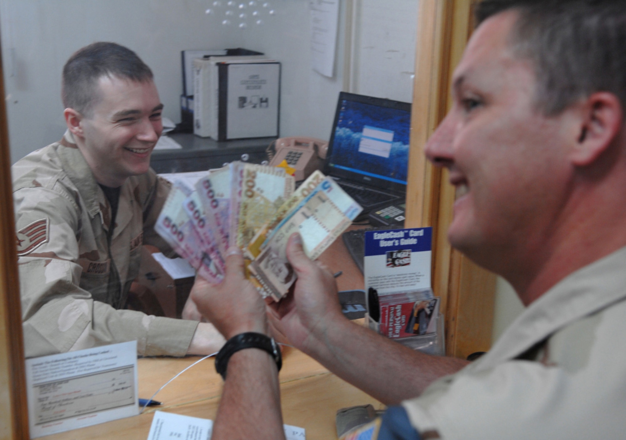 MANAS AIR BASE, KRYGYZ REPUBLIC--Staff Sgt. Joseph Crossan, 376th Air Expeditionary Wing finance services technician, is all smiles as he exchanges dollars for som, the local Krygyz currency, to Master Sgt. Larry Laney, 376th AEW Force Protection office. Unlike many other forward operating bases, Manas allows deployed members the opportunity to go off base to visit local orphanages and schools, community centers, restaurants. But before they can go off base, servicemembers must first visit finance customer service representatives to exchange dollars for som.  (Air Force photo / Tech. Sgt. Michael Voss)