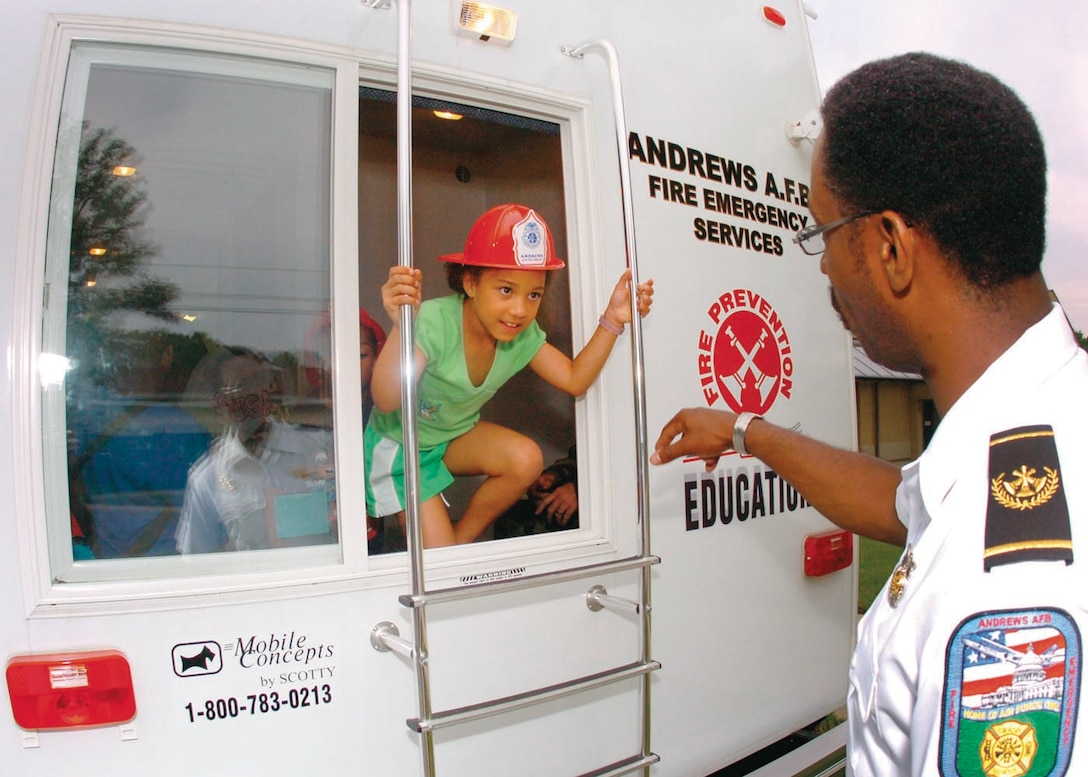 Imani Truss, 7, emerges from the 316th Civil Engineer Squadron Firefighter’s Fire Safety House trailer as Christopher Parks, 316 CES assistant fire chief prepares to instruct her on how to descend down the ladder.
Imani is the daughter of Tech. Sgt. Susan Padilla-Roman, 79th Medical Surgical Squadron Women’s Health Clinic NCO in charge.  (USAF photo by Bobby Jones)