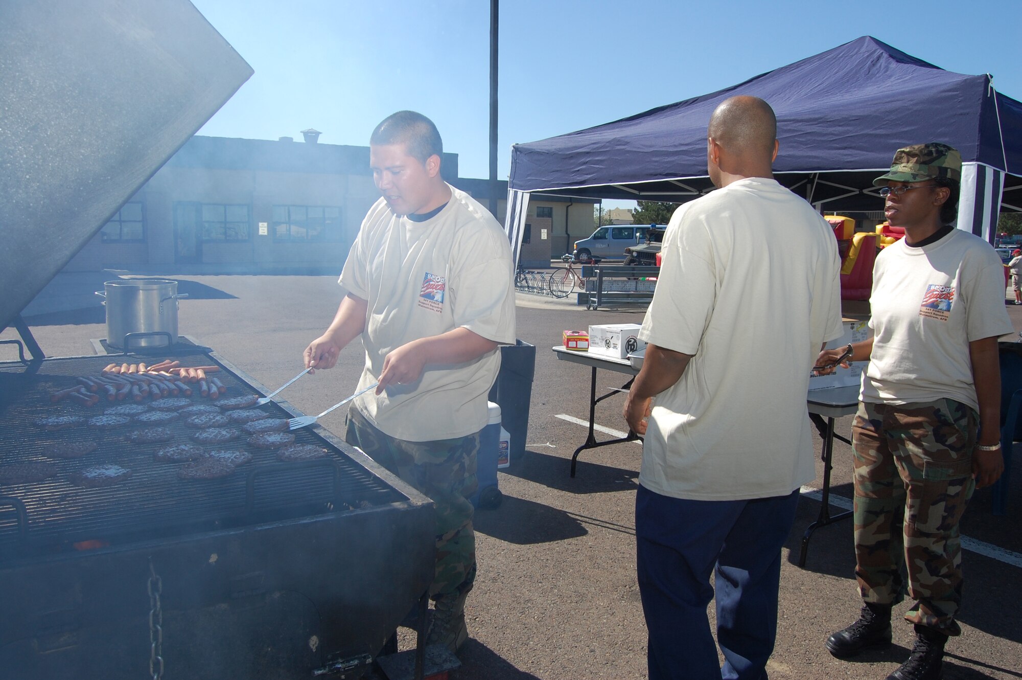 Airman 1st Class Ed Dunn, 341st Force Support Squadron, grills hamburgers and hot dogs as Tech. Sgt. Ladale Evans and Staff Sgt. Michaela Maximin, 341st FSS, look on. Burgers and hot dogs were sereved during the Youth Programs Center's Be Our Guest deployment simulation Aug. 5. (U.S. Air Force photo/Airman 1st Class Emerald Ralston)