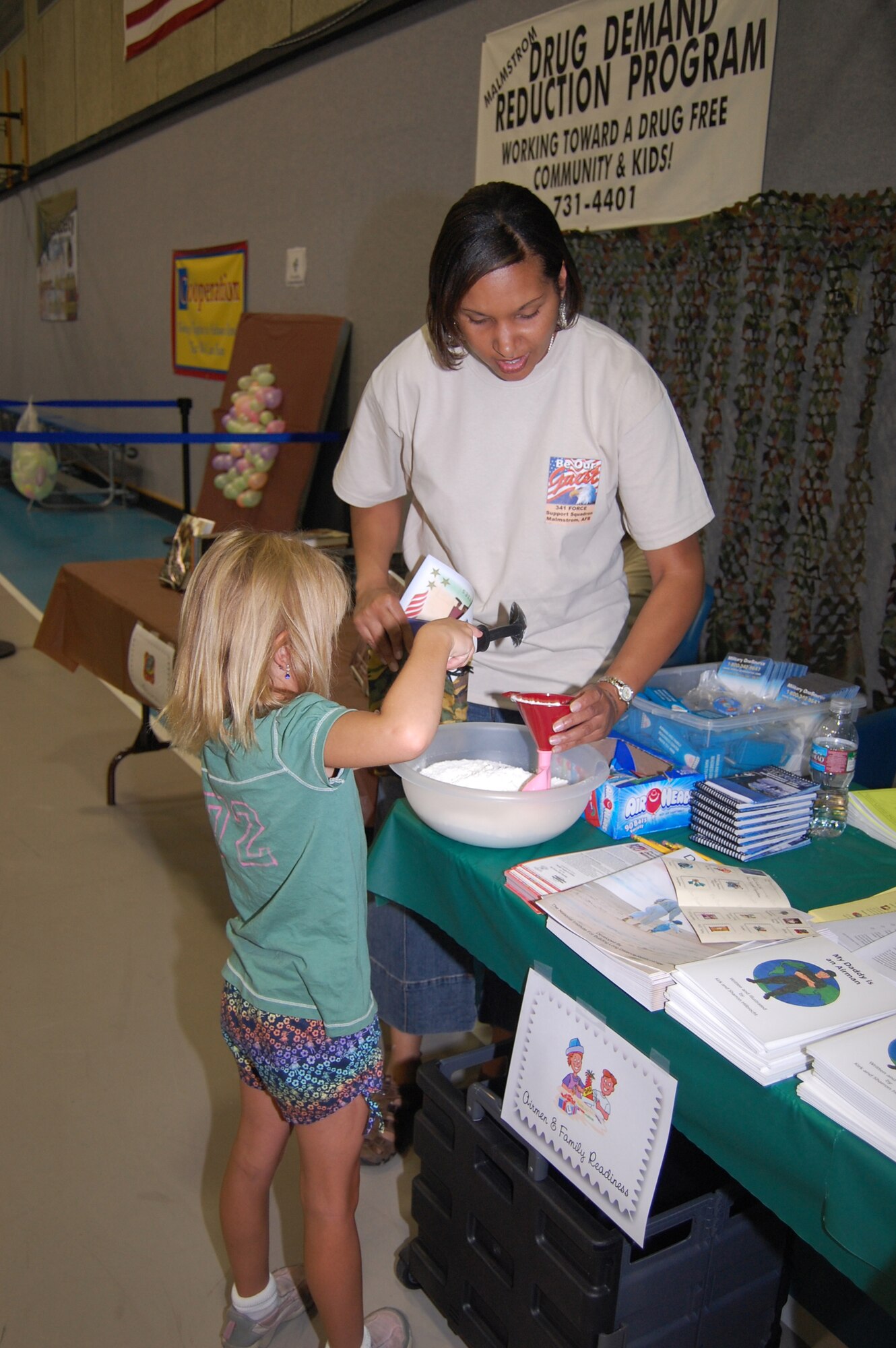 Karan Killiard, 341st Force Support Squadron, helps Little Warrior Alaina, 7, make a stress ball out of flour and a balloon during a mock deployment held at the Youth Programs Center Aug. 5. (U.S. Air Force photo/Airman 1st Class Emerald Ralston)