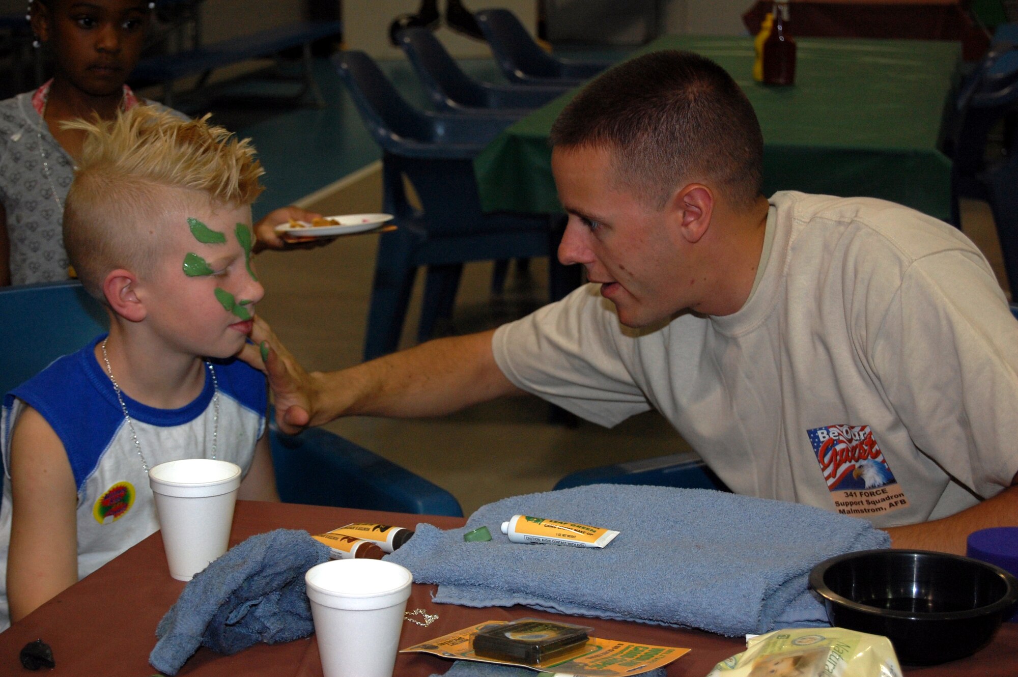 Airman James Demarsico, 341st Security Forces Squadron, paints the face of Little Warrior Braden, 7, during the Youth Programs Center's Be Our Guest mock deployment line Aug. 5. (U.S. Air Force photo/Airman 1st Class Emerald Ralston)