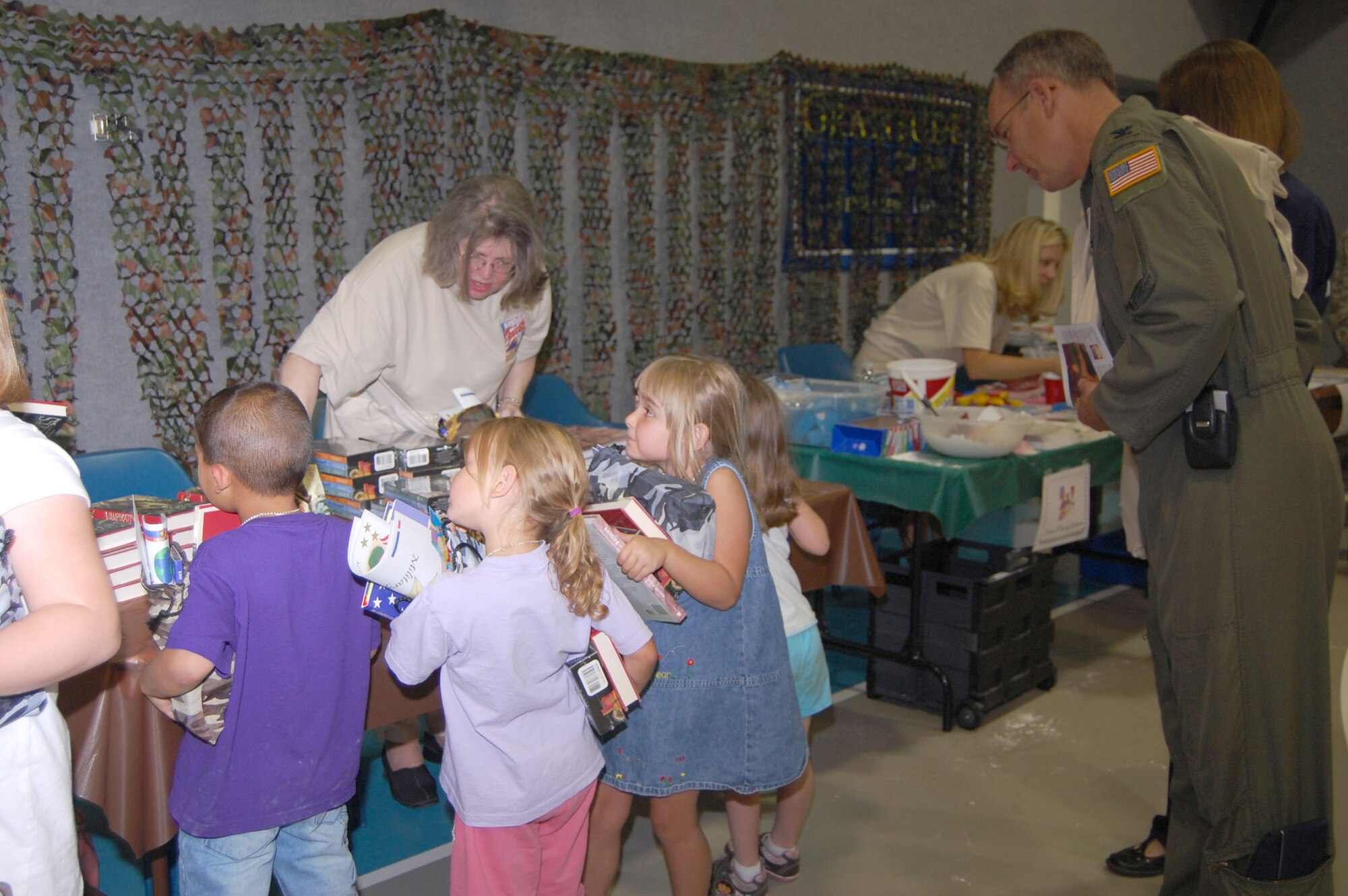 Col. Michael Fortney, 341st Missile Wing commander, looks on as Carol Banas, librarian, hands out books during the Youth Programs Center's Be Our Guest mock deployment line Aug. 5. (U.S. Air Force photo/Airman 1st Class Emerald Ralston)