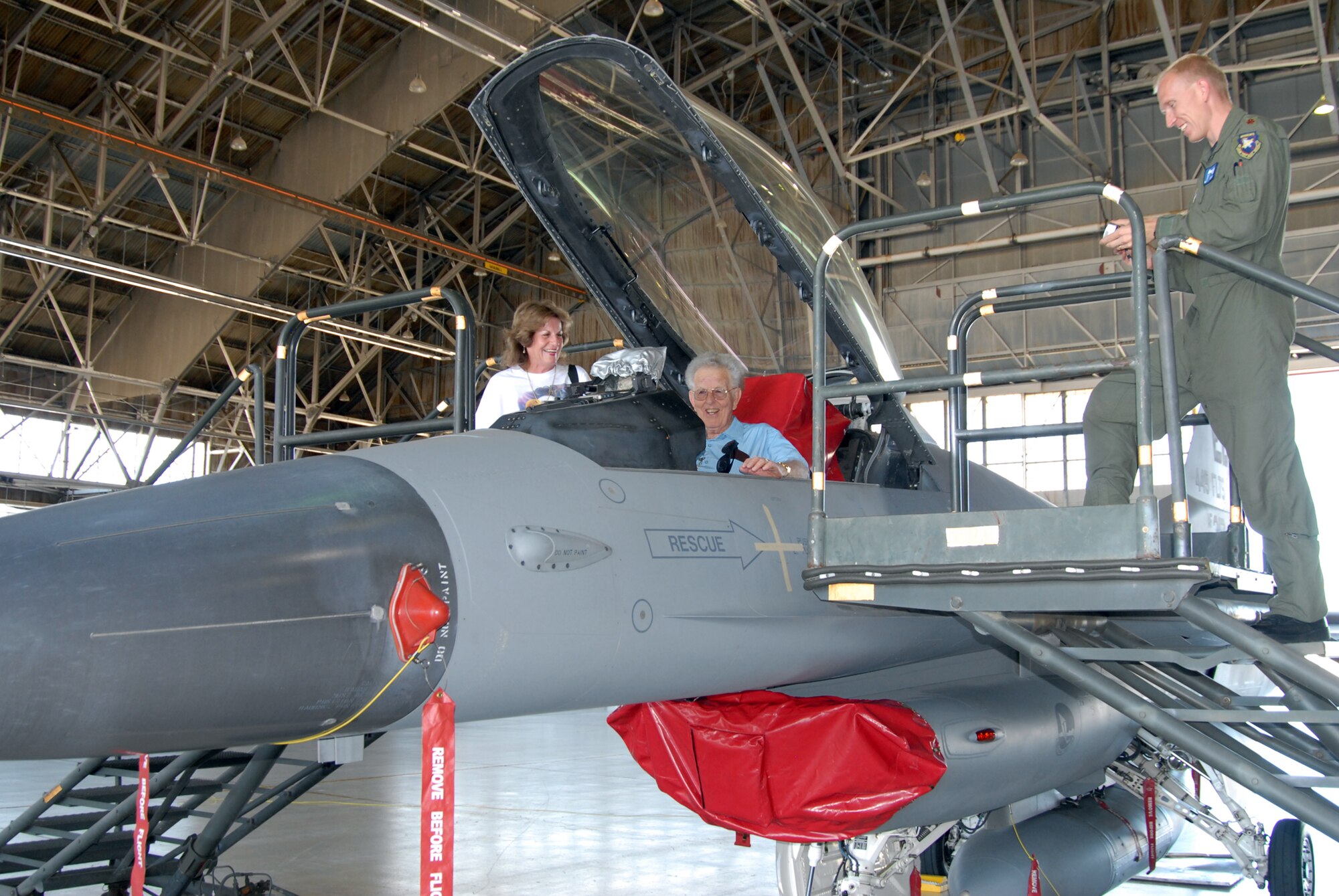 Richard McKenzie (center), a Korean War veteran,  sits in the cockpit of an F-16 Fighting Falcon as part of the Never Too Late program here Aug 1, while Maj. Scott Mclaren (right), 445th Flight Test Squadron weapons and standard evaluation flight commander, and Carolyn Swain, Mr McKenzie's friend, look on. The Never Too Late program is designed to assist elder citizens in making their dreams come true. 