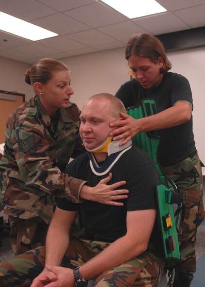 MOODY AIR FORCE BASE, Ga. – Tech. Sgt. Charity Gerner, 23rd Aerospace Medical Squadron NCO in-charge of ambulance dispatch, and Staff Sgt. Erin Grimme, 75th Fighter Squadron independent duty medical technician, lean forward Master Sgt. Robert Karbach, 820th Security Forces Group independent duty medical technician, to slide a Kendrick extraction device behind his back here Aug. 6. The KED is used to keep accident victim’s head and back stabilized to minimize further injury. (U.S. Air Force photo by Airman Joshua Green)   