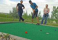 MINOT, N.D. -- Airman 1st Class Justin Palmer, 5th Aircraft Maintenance Squadron crew chief, attempts to sink a putt as Senior Airman Stephanie Campbell, 5th Communications Squadron visual imagery intrusion detection systems technician, and Airman 1st Class Natasha Ashley, 742nd Missile Squadron, missile alert facility chef, watch the ensuing play at Valleyview Falls Mini-Golf-Go Aug. 9. (U.S. Air Force photo by Airman 1st Class Benjamin Stratton)