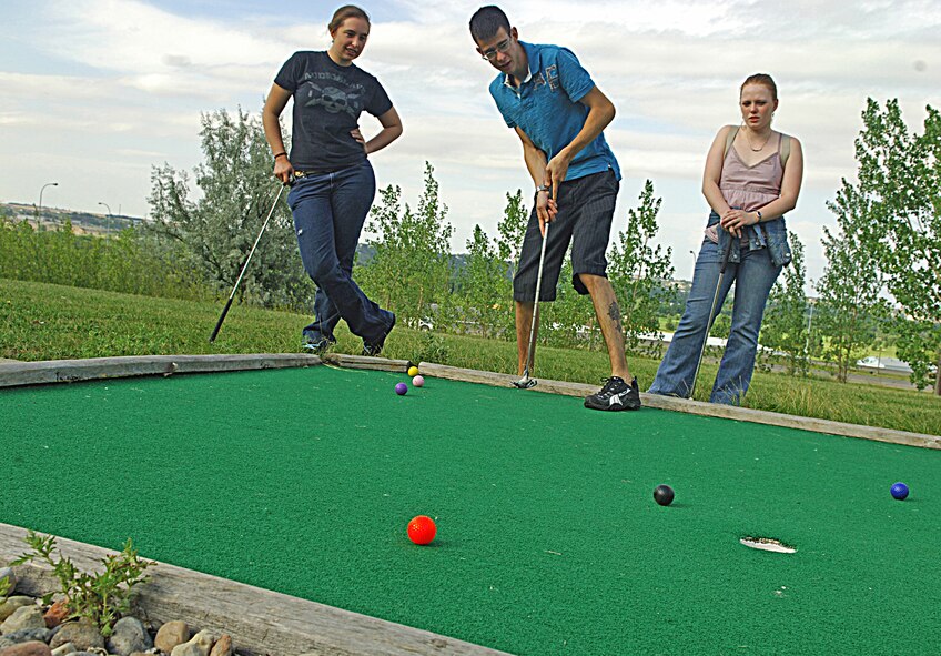 MINOT, N.D. -- Airman 1st Class Justin Palmer, 5th Aircraft Maintenance Squadron crew chief, attempts to sink a putt as Senior Airman Stephanie Campbell, 5th Communications Squadron visual imagery intrusion detection systems technician, and Airman 1st Class Natasha Ashley, 742nd Missile Squadron, missile alert facility chef, watch the ensuing play at Valleyview Falls Mini-Golf-Go Aug. 9. (U.S. Air Force photo by Airman 1st Class Benjamin Stratton)
