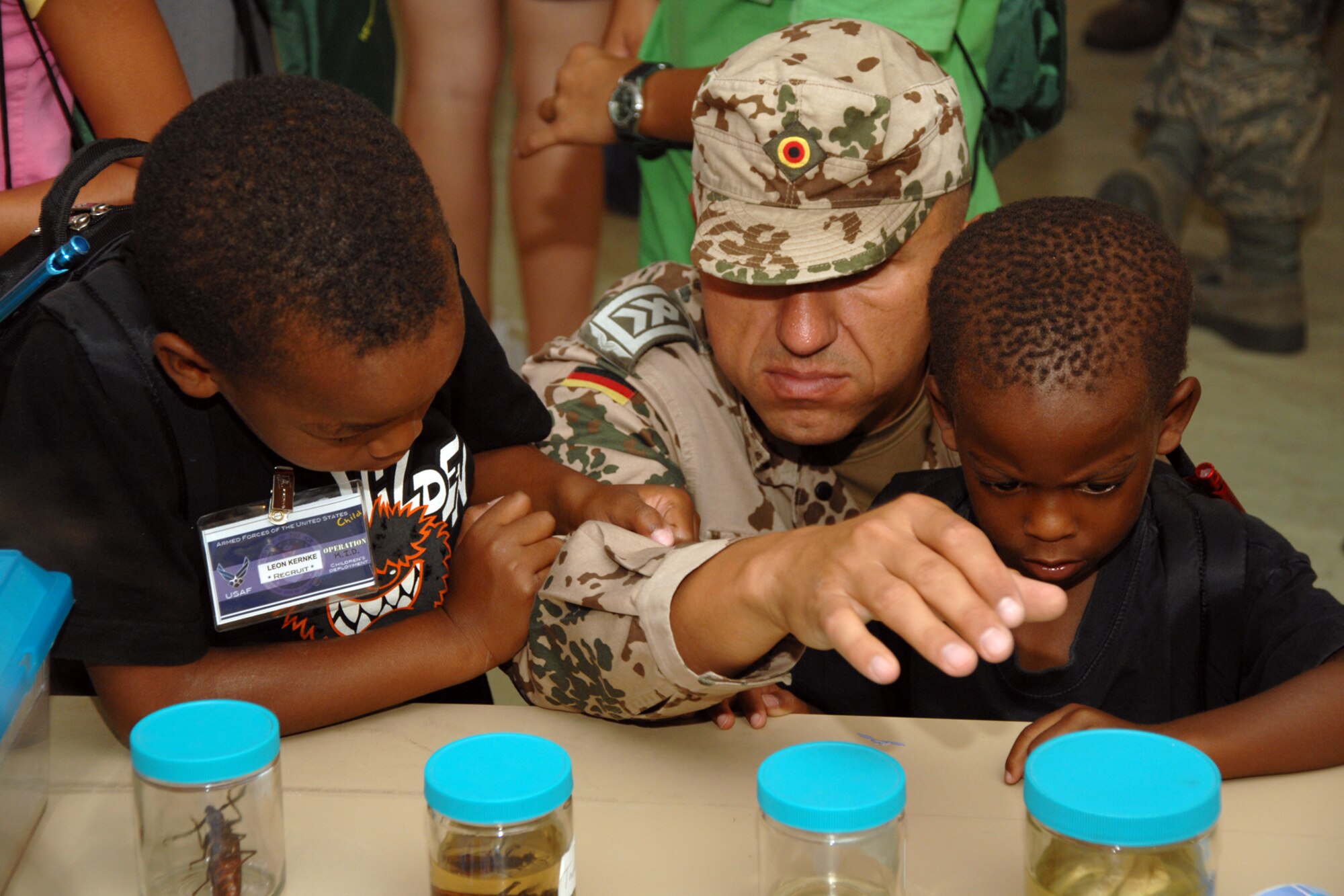 German air force Senior Master Sgt. Roland Kernke, Leon Currie, 6, and Niam Kernke, 3, check out bug displays at the 49th Medical Group educational station during the Operation K.I.D. mock deployment Aug. 7 at Holloman Air Force Base, N.M. After the mock deployment to Balad Air Base, Iraq, children and parents returned to Hangar 301 for the Hail and Farewell ceremony. (U.S. Air Force photo/Airman 1st Class Jamal D. Sutter)