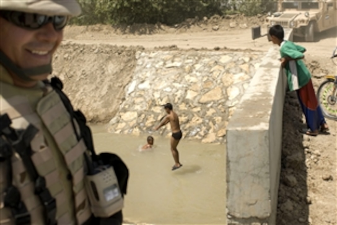 Col. Walter Mauricio Arévalo, an El Salvador battalion commander, turns from inspecting a newly completed canal bridge in Numaniyah near Forward Operating Base Delta, Iraq, as boys jump into the water to beat the heat, Aug. 8, 2008.